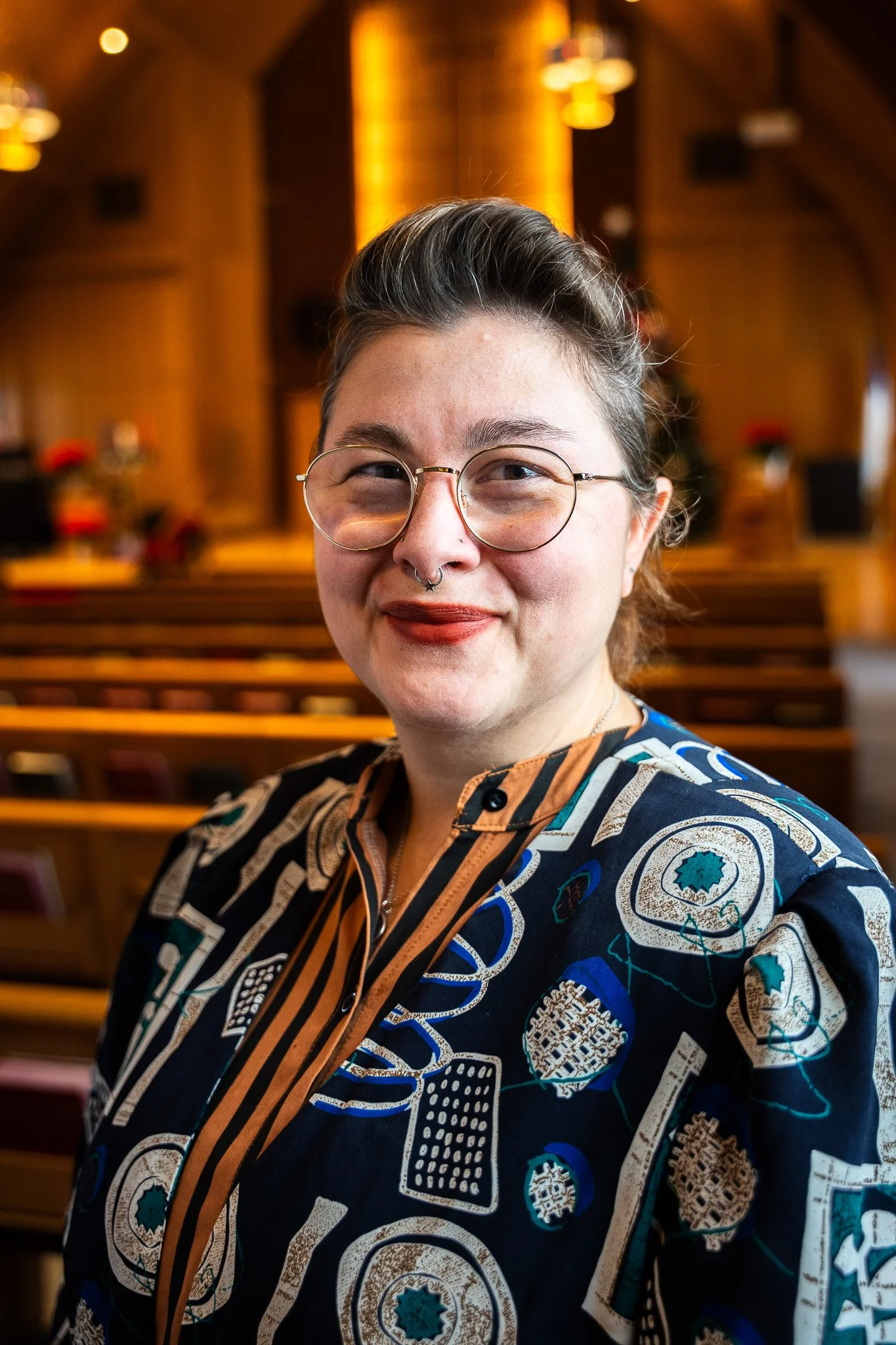 A woman with curly brown hair smiling at the camera, wearing a dark blue blouse with a textured pattern.