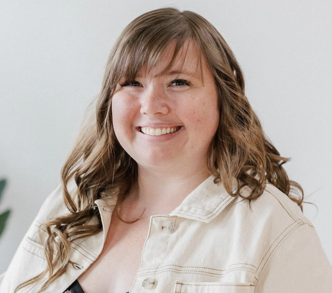 A woman with long wavy brown hair and a light-colored jacket smiling at the camera.