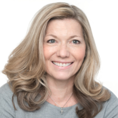 A woman with long blonde hair, smiling, wearing a light gray top.