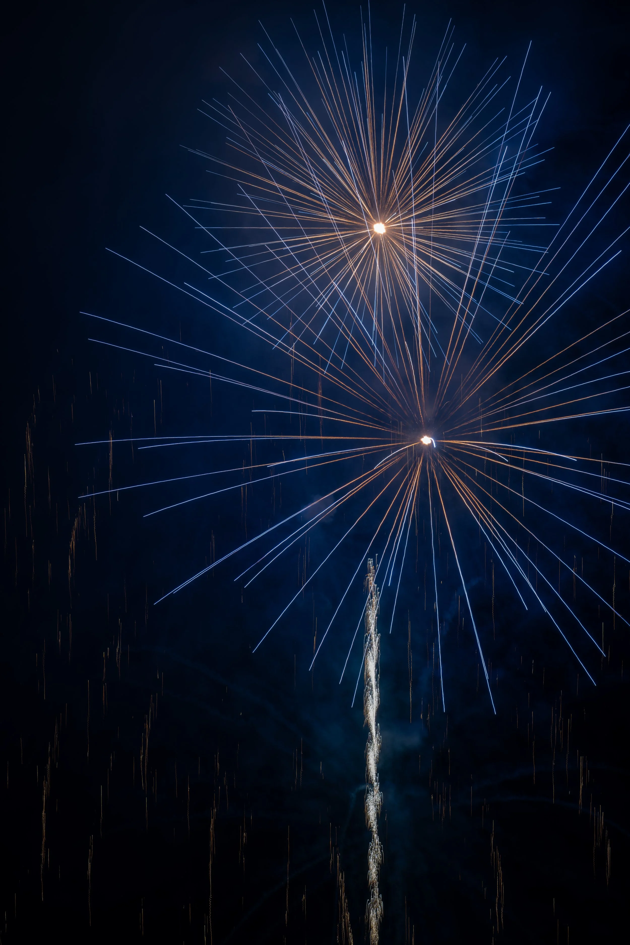 Fireworks exploding in the night sky with bright streaks of blue and orange light.