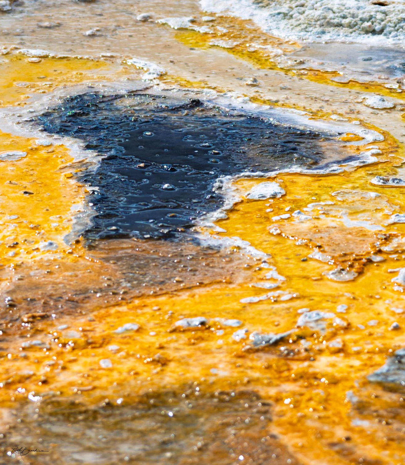Close-up of a geothermal hot spring with colorful mineral deposits and bubbling dark water.