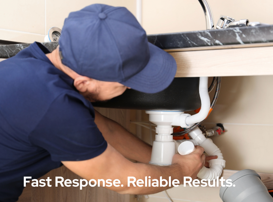 A plumber fixing a sink leak under a kitchen sink with tools and pipes.