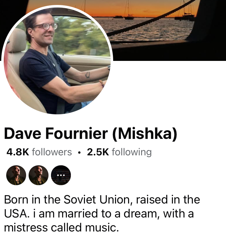 Profile picture of a man smiling while driving a car, with a sunset view over the water and boats in the background.