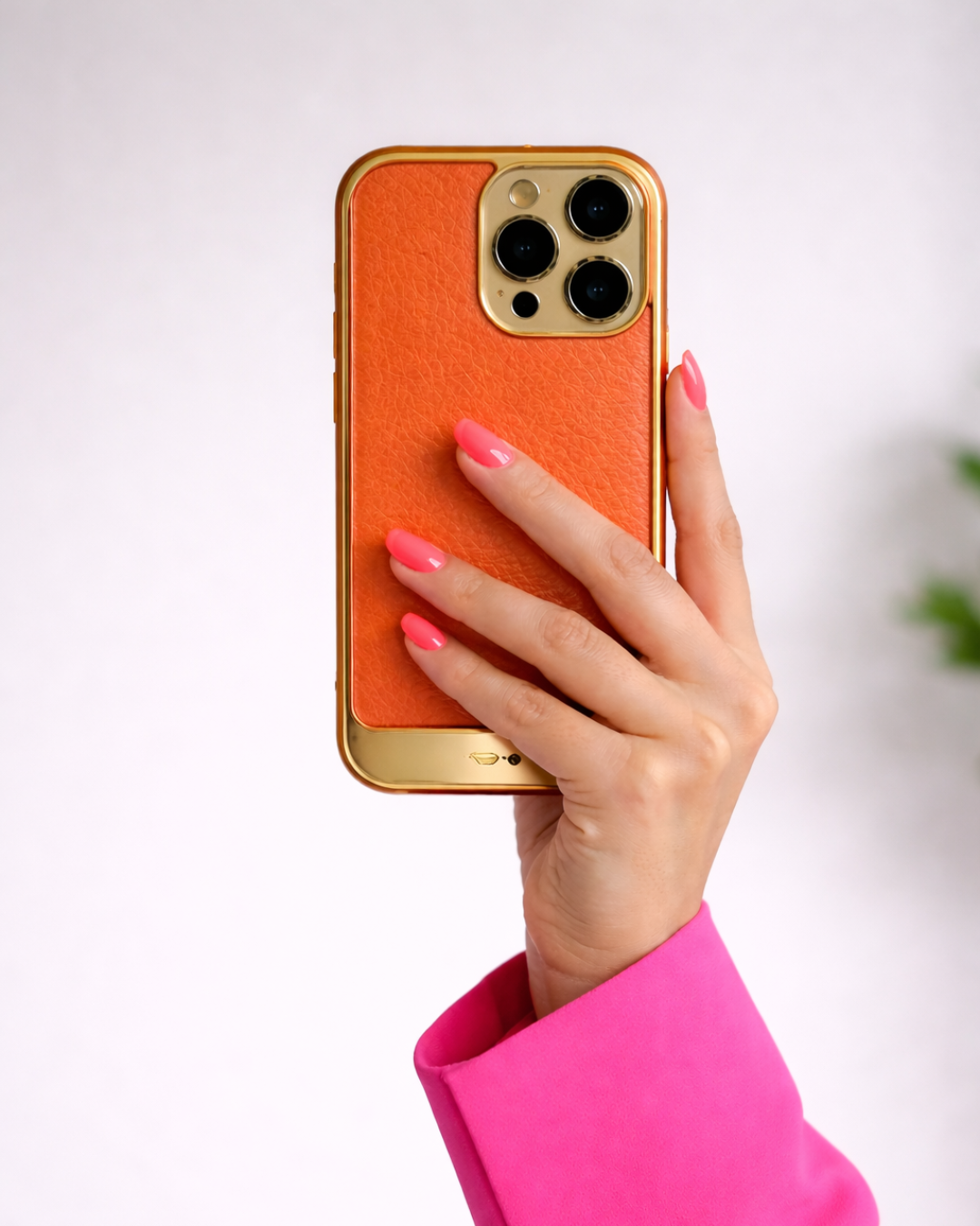 A hand with painted pink nails holding an orange and gold smartphone against a plain white background.