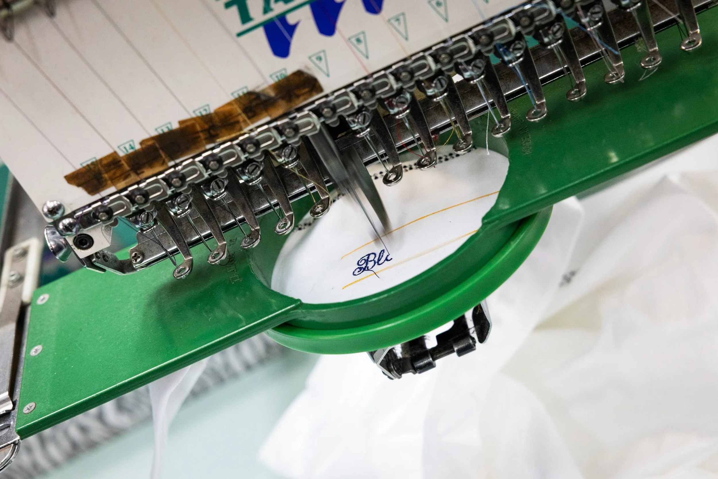 Close-up of an embroidery machine stitching the words 'Blue' on a white fabric.
