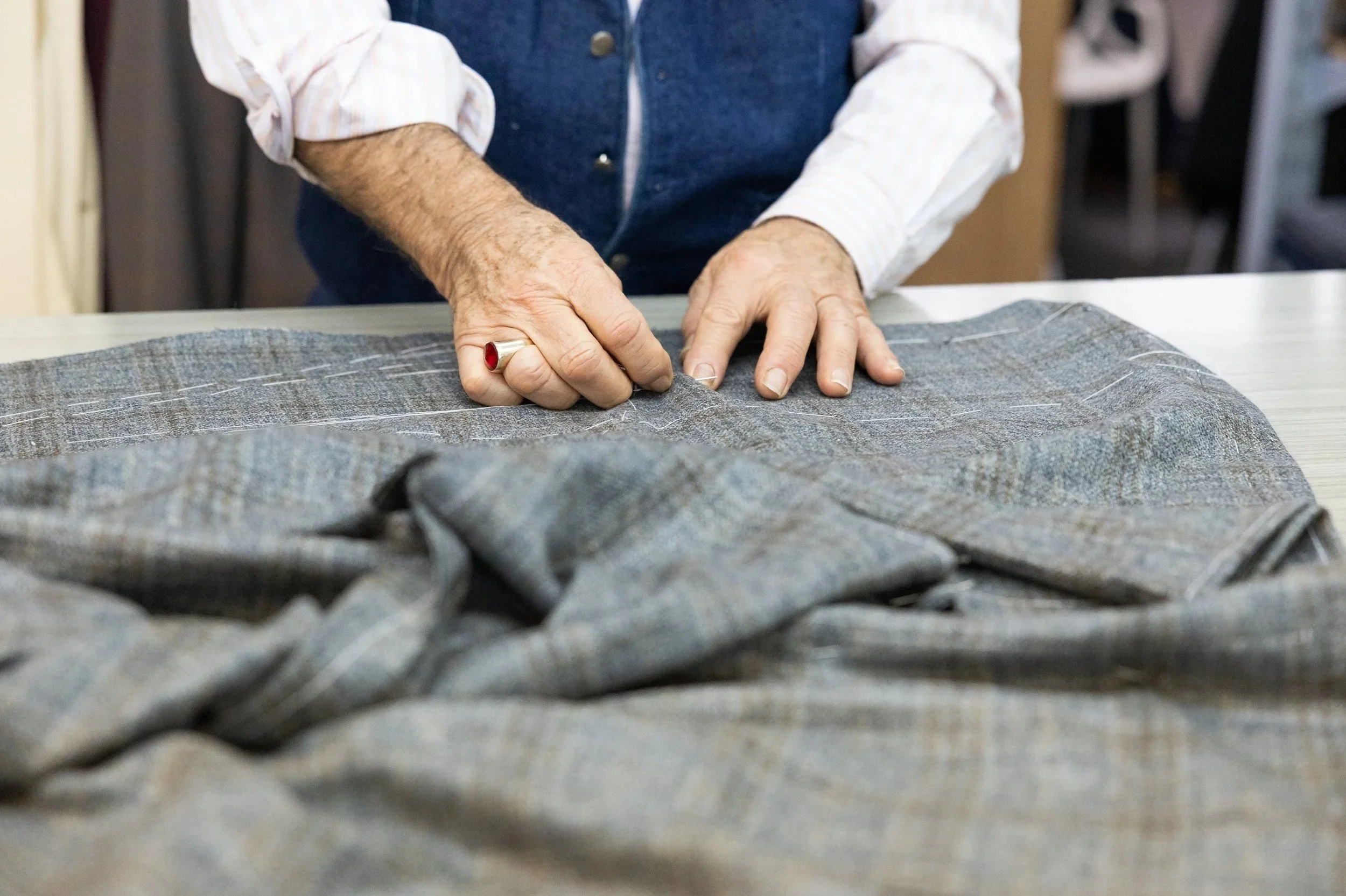 A person making tailoring or sewing adjustments on a gray plaid fabric, using white chalk to mark the fabric on a table.