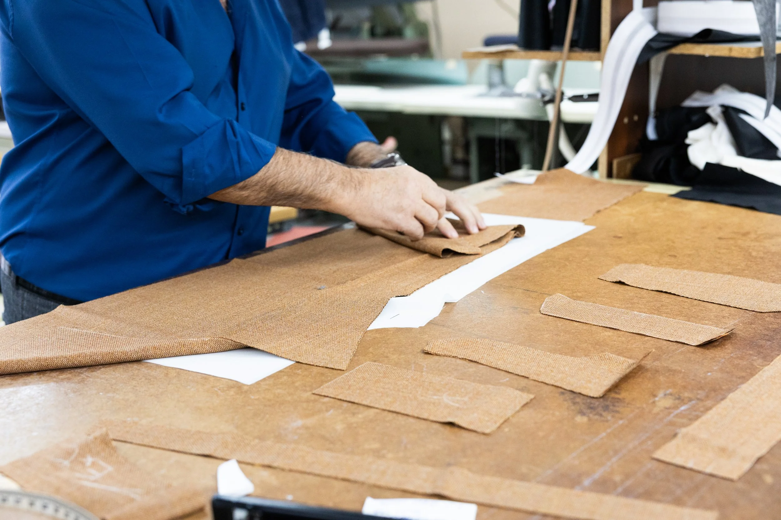 Person in blue shirt working with leather pieces on a worktable.