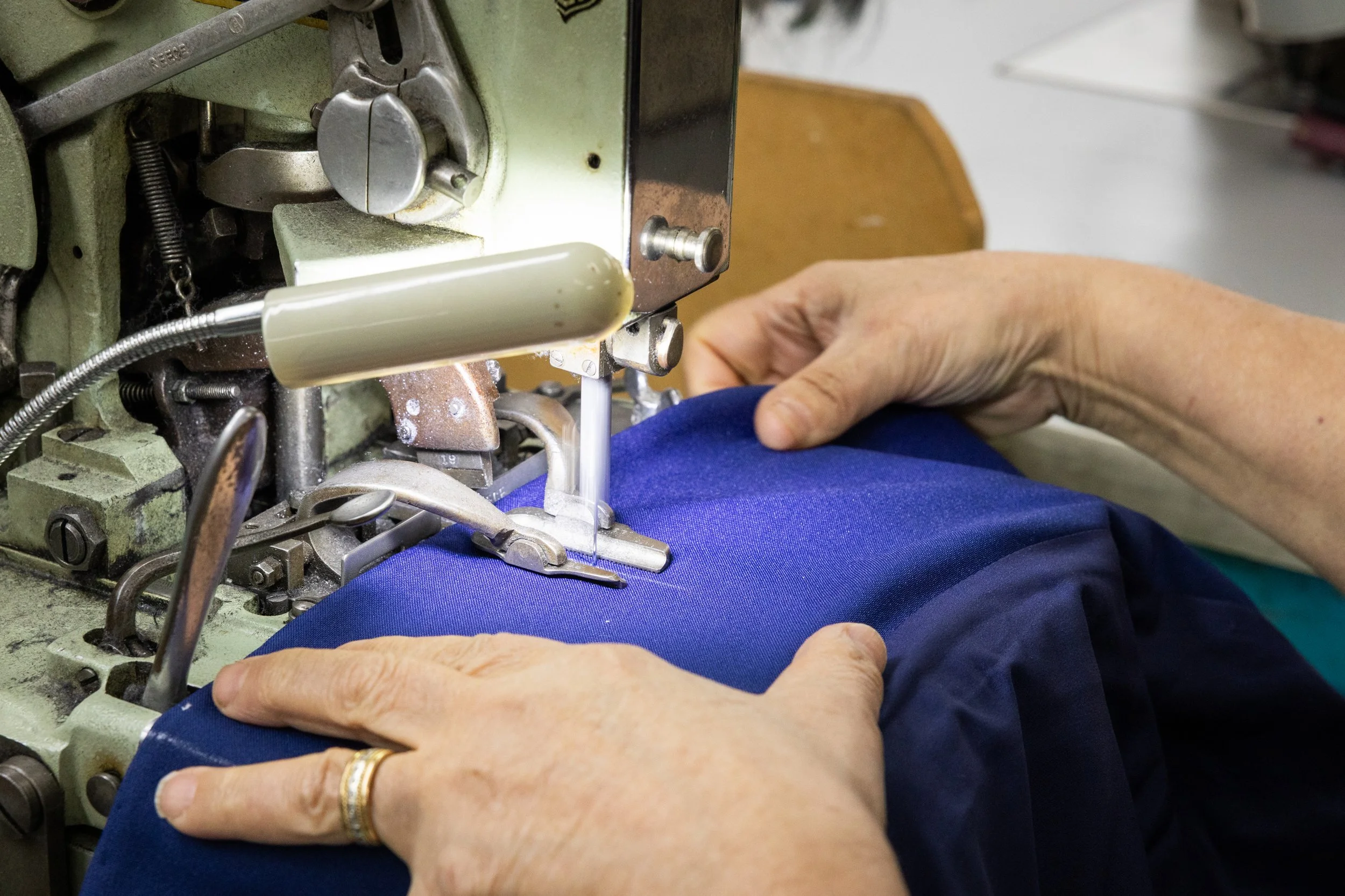 Close-up of a person sewing blue fabric on a vintage industrial sewing machine.