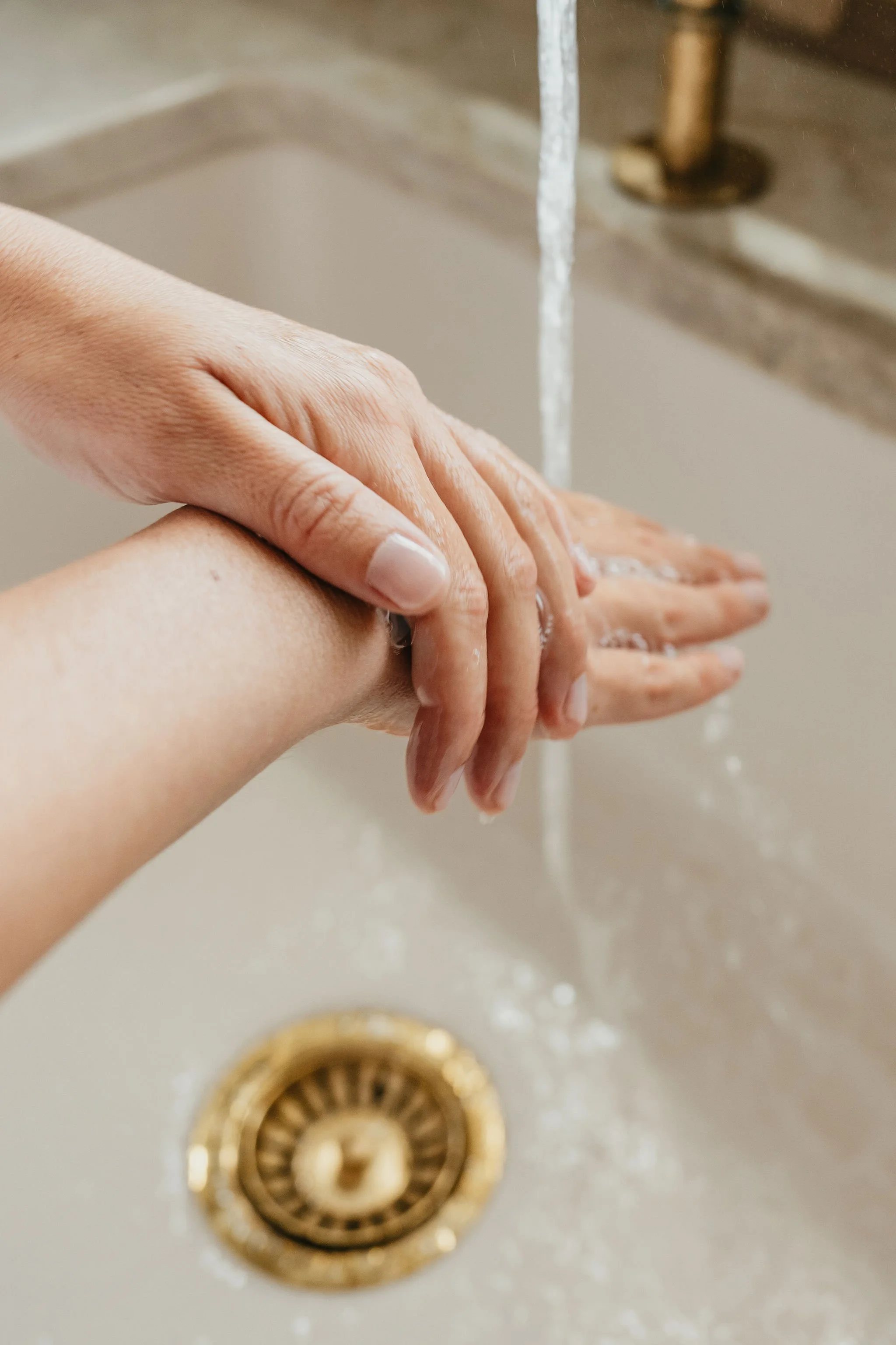 Person washing hands with water at kitchen sink.
