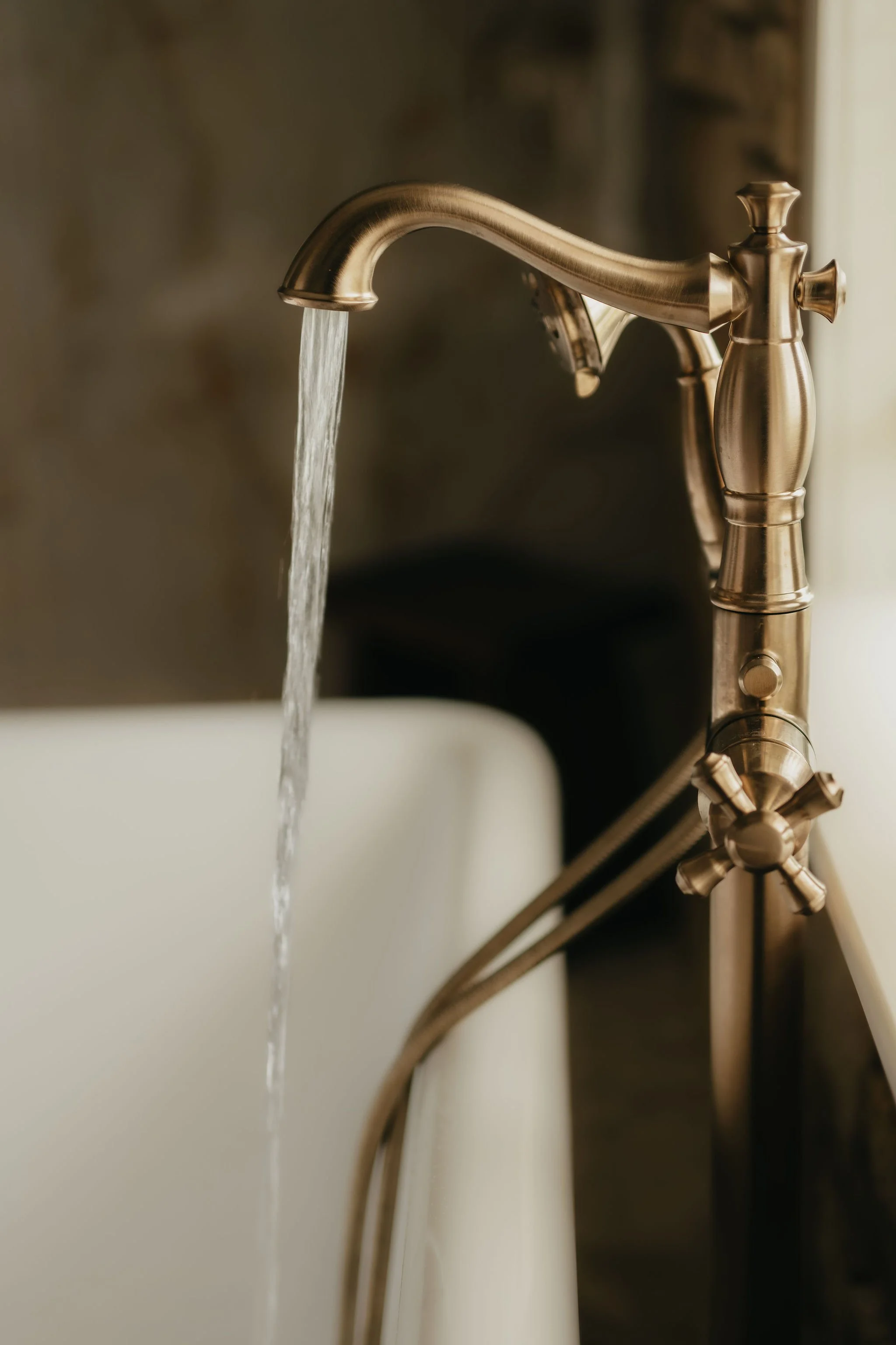 Close-up of a brass kitchen faucet with water running into a white sink.