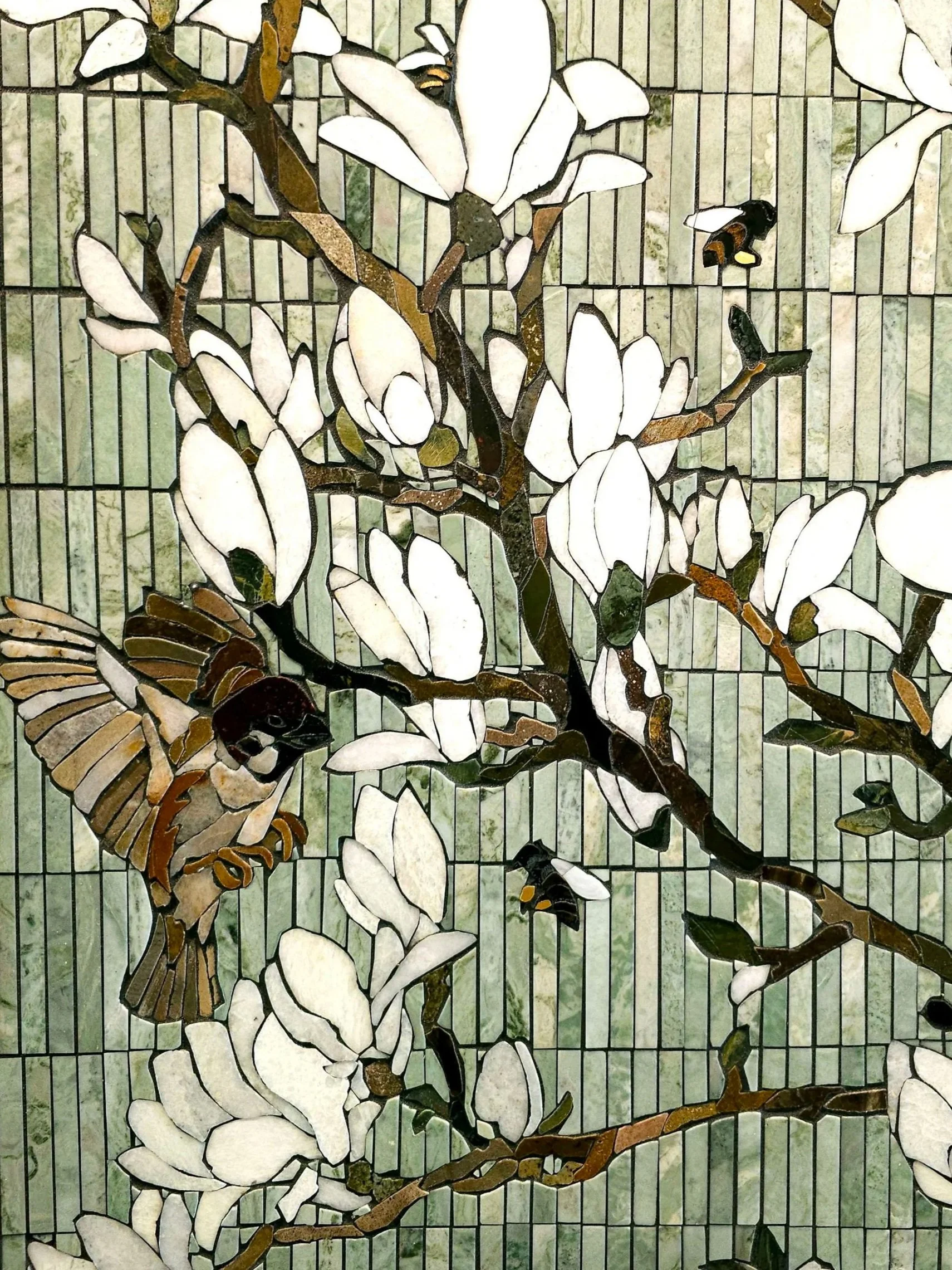 A stained glass window depicting a branch with white magnolia flowers, a hummingbird, and bees.