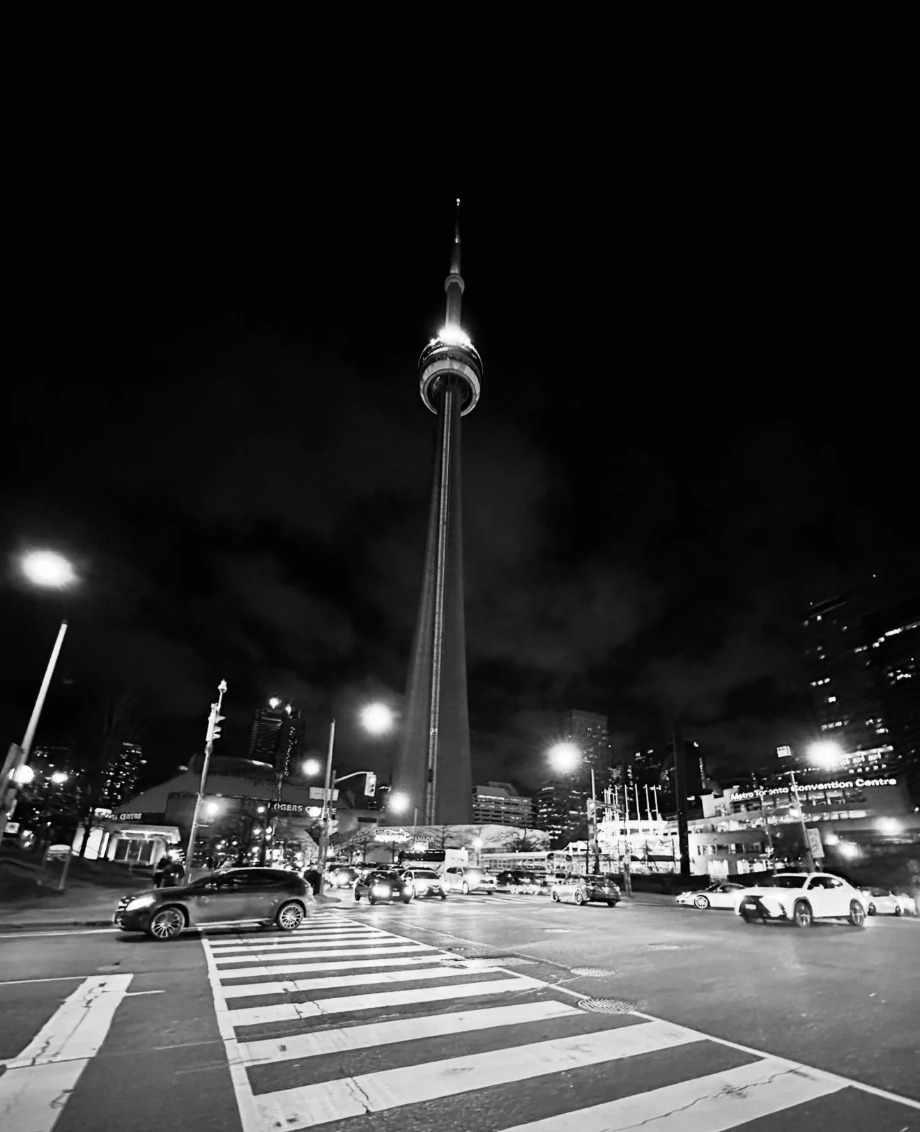 Nighttime view of the CN Tower in Toronto, Canada, with cars and streetlights in the foreground.