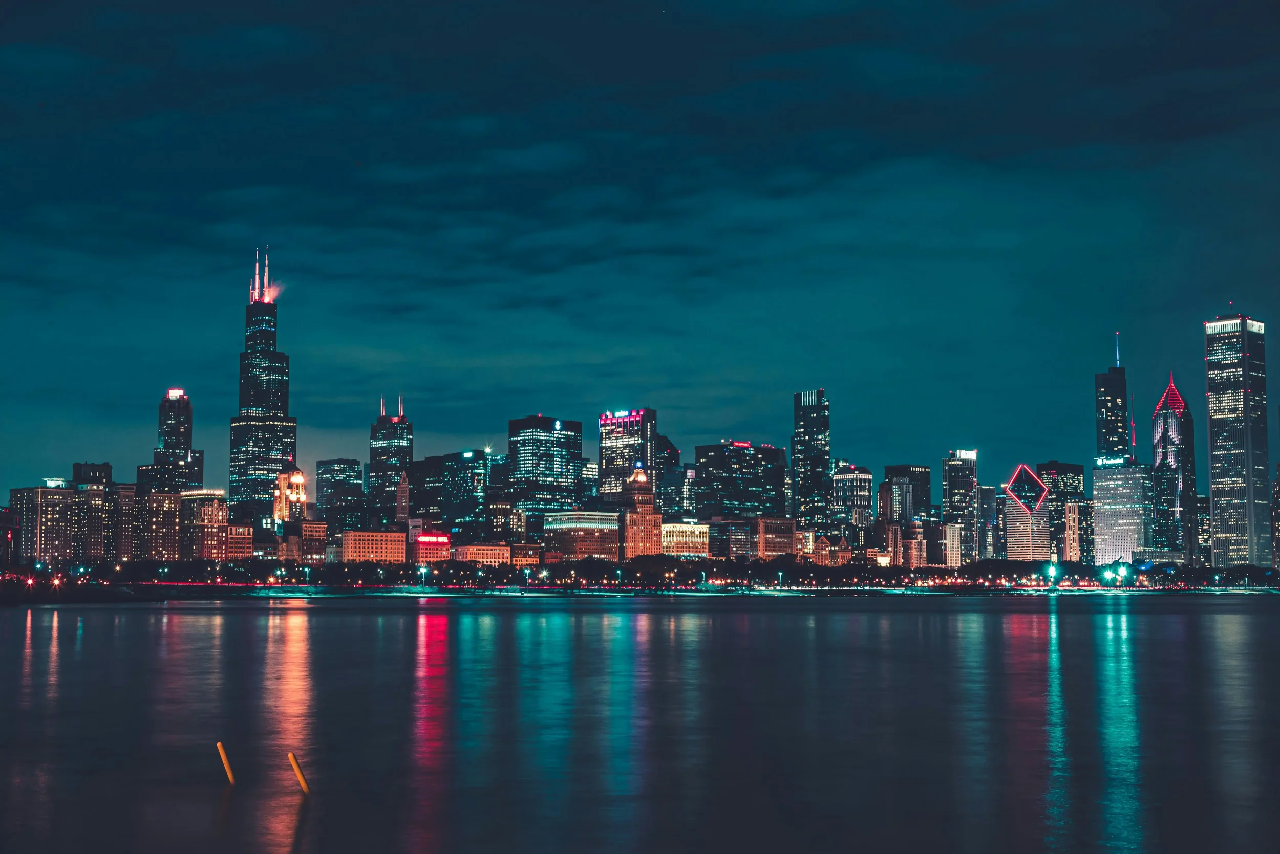 Nighttime view of the Chicago skyline with illuminated skyscrapers reflected on the water.