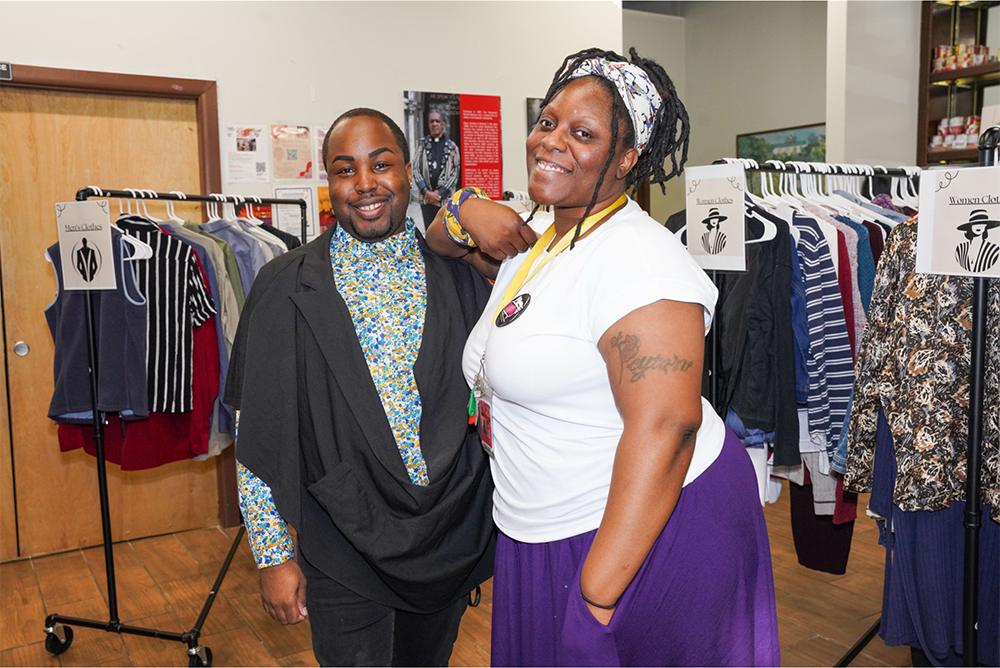 Two smiling individuals posing inside a clothing store, surrounded by racks of clothes.