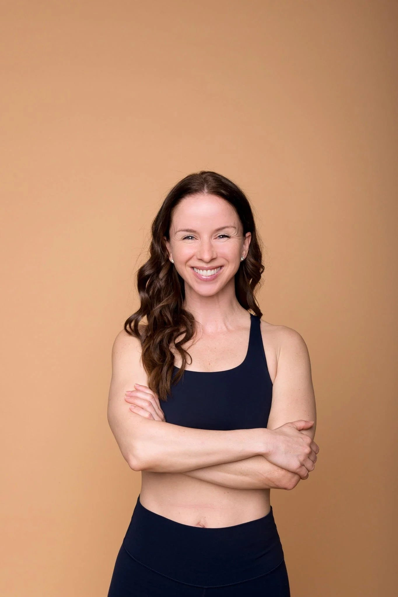 Smiling woman with wavy brown hair in athletic wear against beige background.