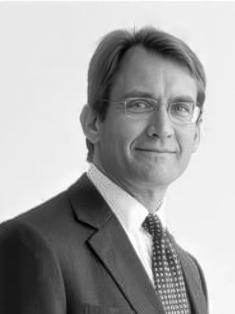 Black and white portrait of a middle-aged man in a suit with glasses, smiling.
