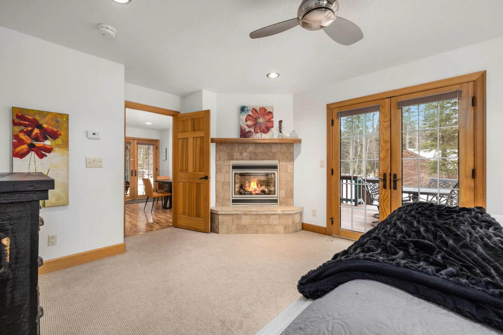 Living room with a fireplace, sliding glass door to a deck, beige carpet, white walls, wooden accents, and a TV with a black blanket over it.