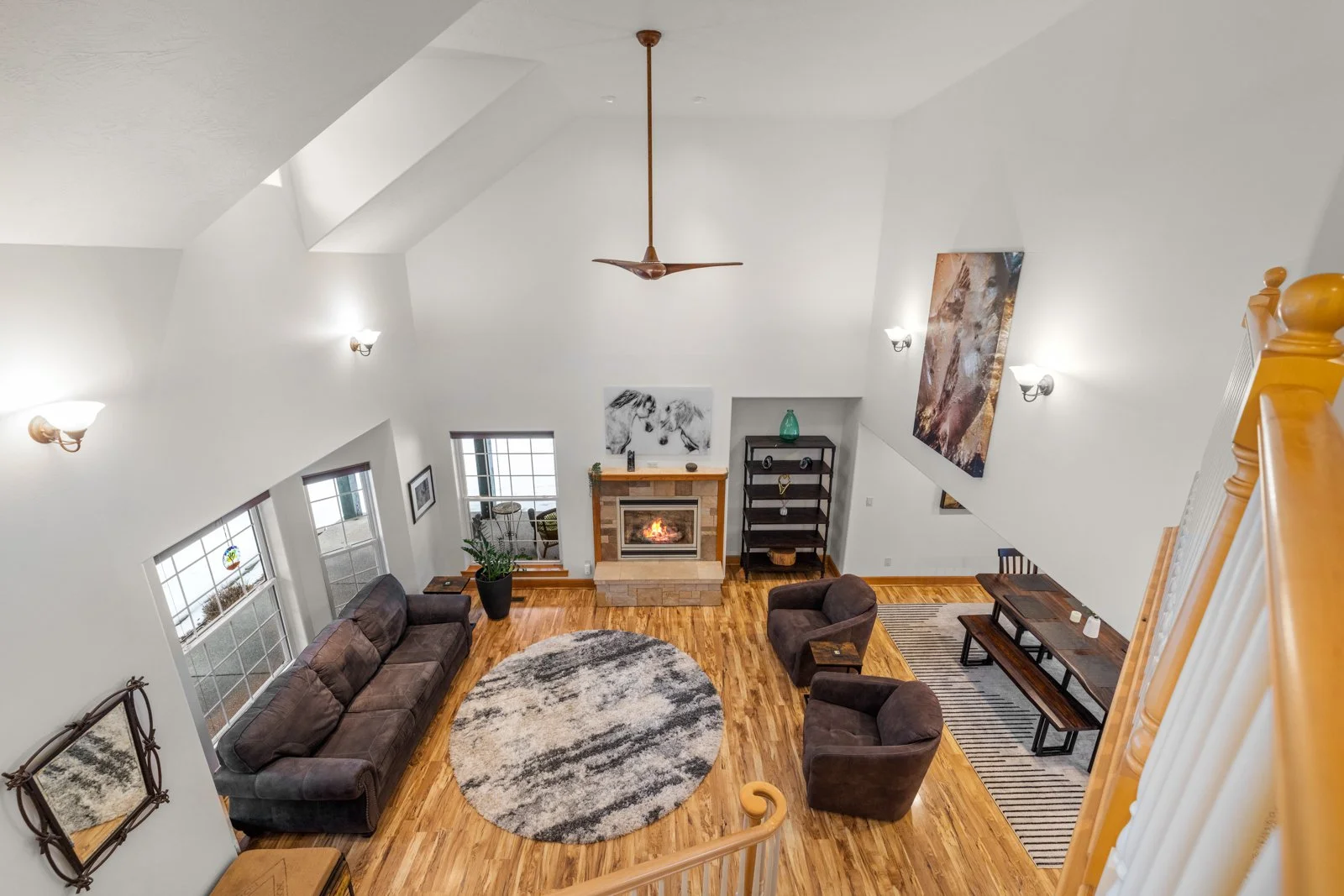 Living room with brown sofas, armchairs, a fireplace, large windows, and wall-mounted lights.