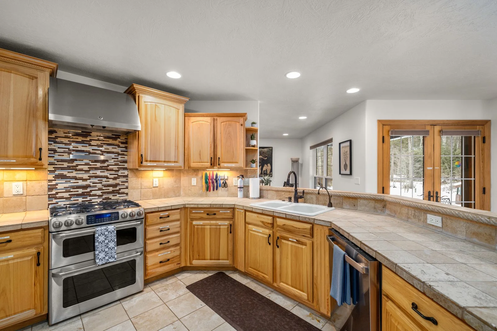 Kitchen with wooden cabinets, a stainless steel stove, a tile backsplash, a double sink, and sliding glass doors leading outside.