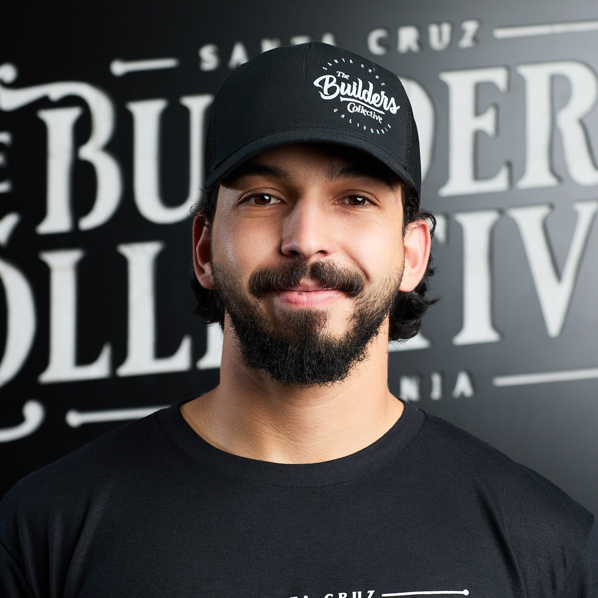A smiling man with red hair and beard standing in front of a wall with large white text that reads 'Santa Cruz' and 'Bubbers'.
