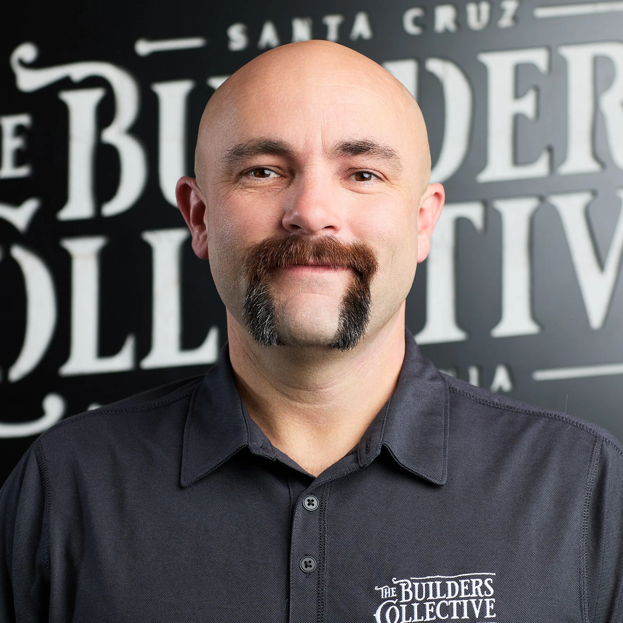 A bald man with a mustache and goatee wearing a black shirt with 'The Builders Collective' logo, standing in front of a black background with white text.