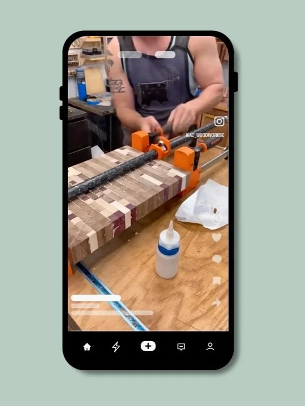 A person using a clamp to hold a wooden block with various colored wood pieces glued together on a workbench, with a bottle of glue and other woodworking tools nearby.