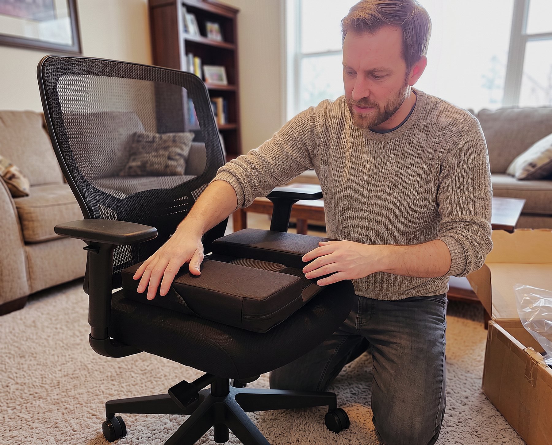 Man kneeling beside an office chair, pressing a Twin Cheeks two-panel cushion into place on the seat