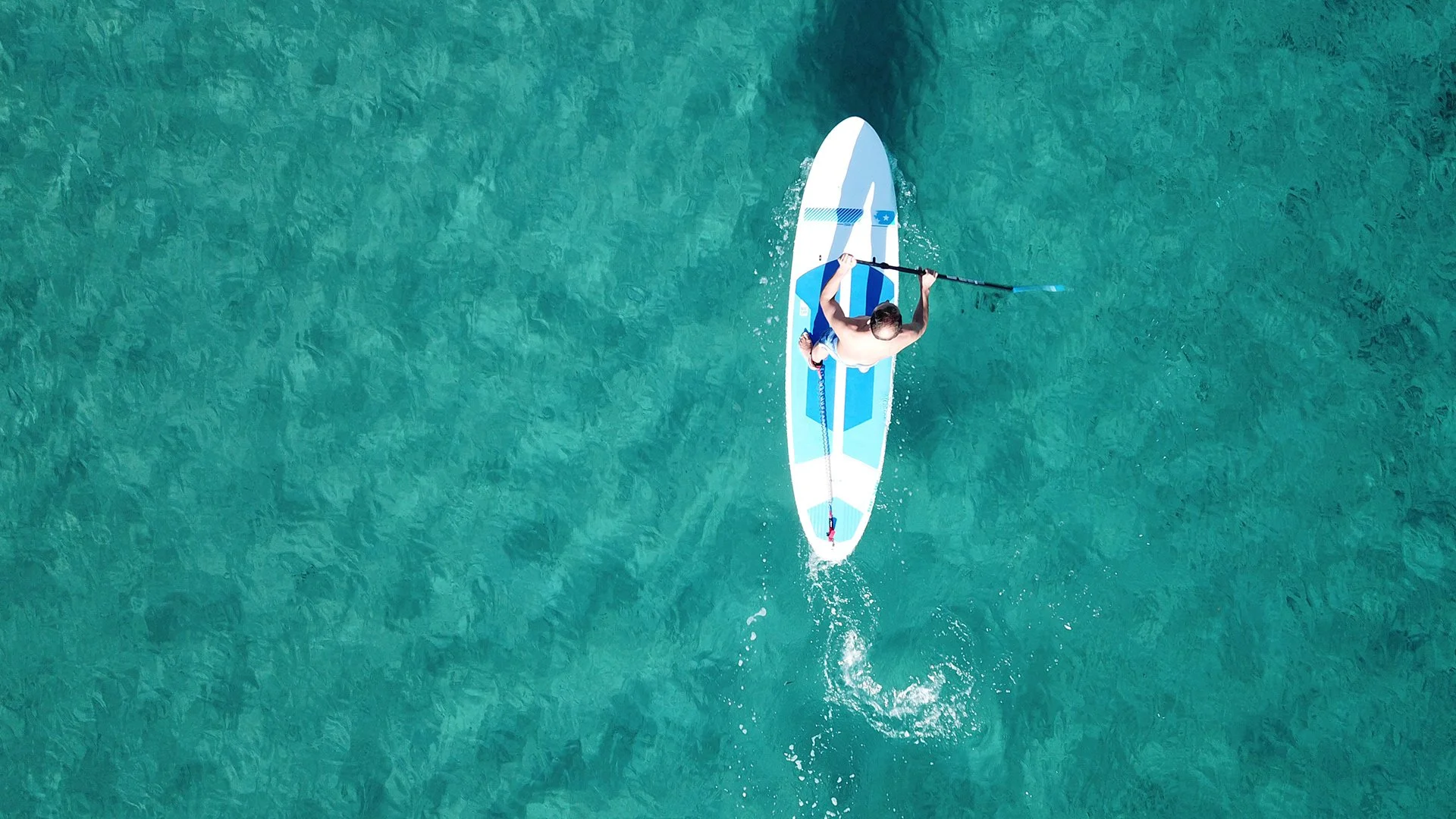 A person paddleboarding on turquoise water, viewed from above.