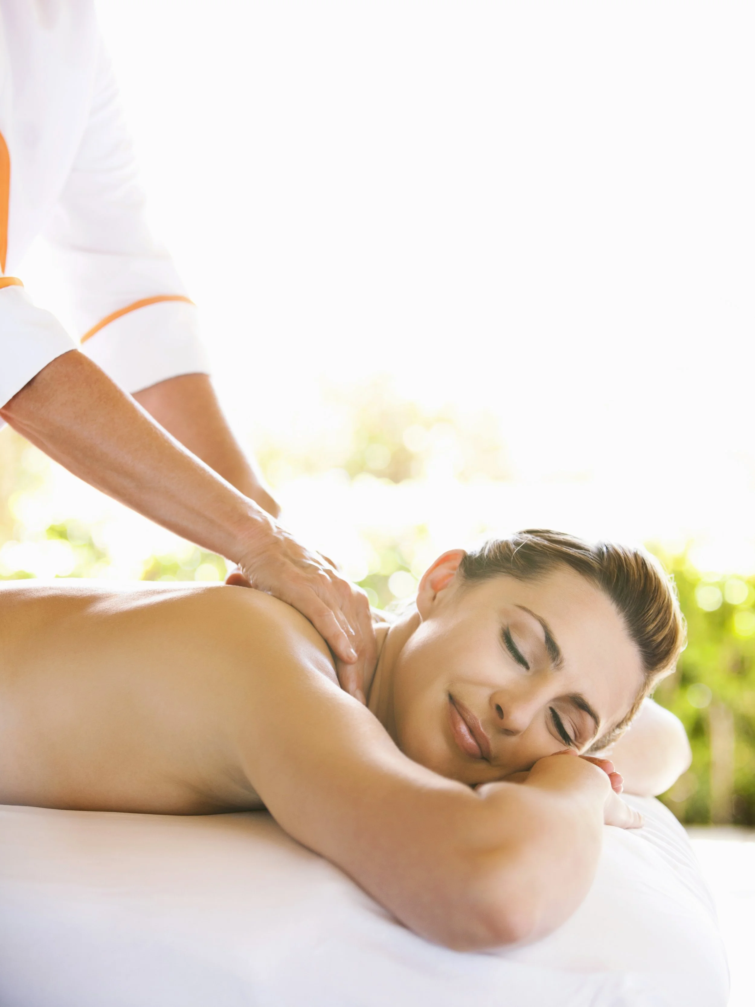 Woman receiving a massage outdoors, lying on a massage table with eyes closed and smiling.