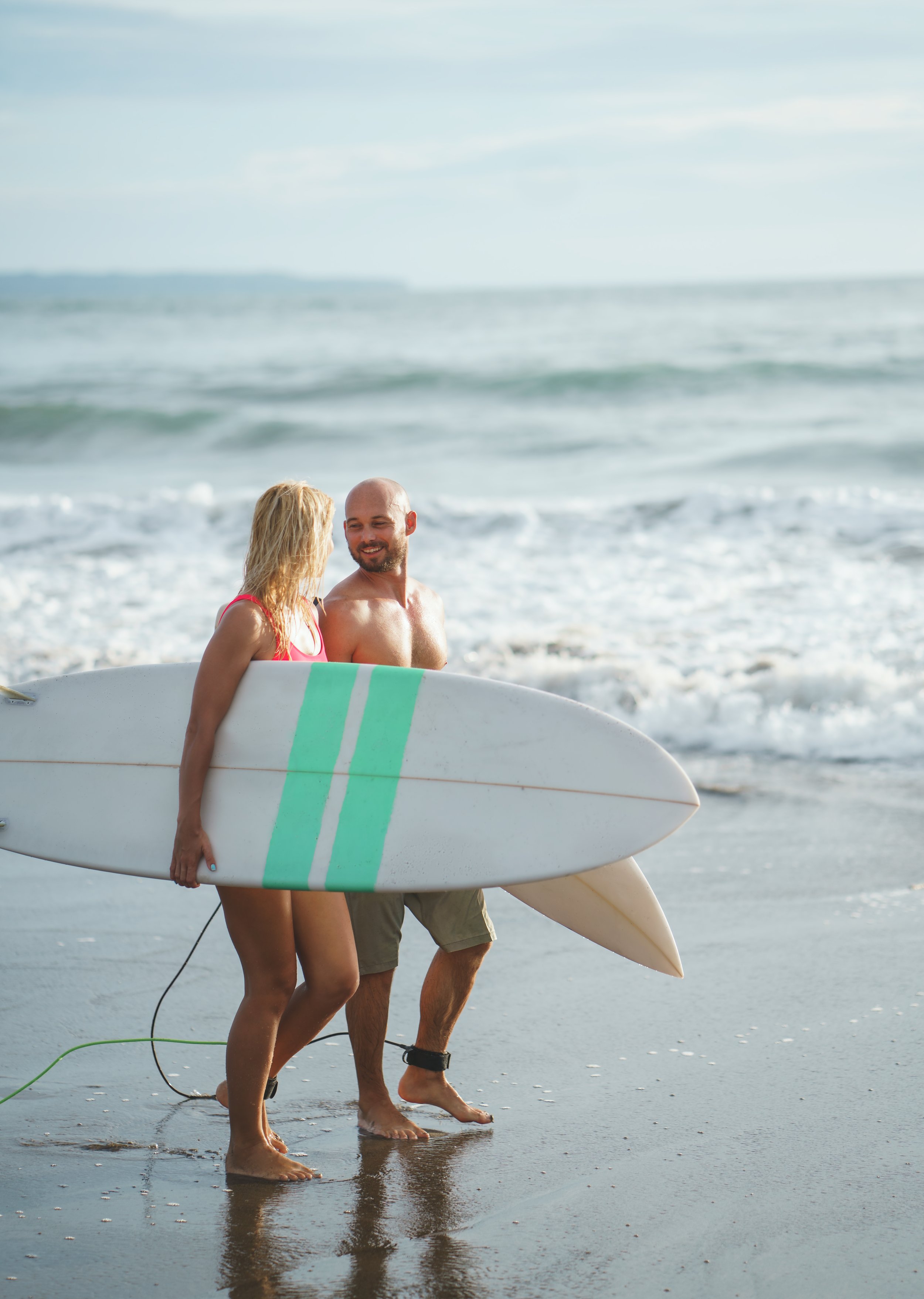 A couple standing at the shoreline with surfboards, about to go surfing at the beach.