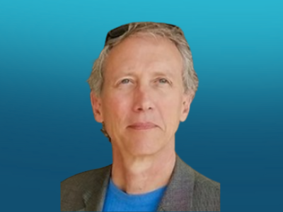 Portrait of a middle-aged man with gray hair, wearing a gray blazer and blue shirt, against a gradient blue background.