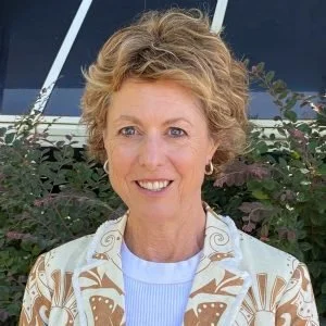 A woman with short, curly blonde hair smiling outdoors.