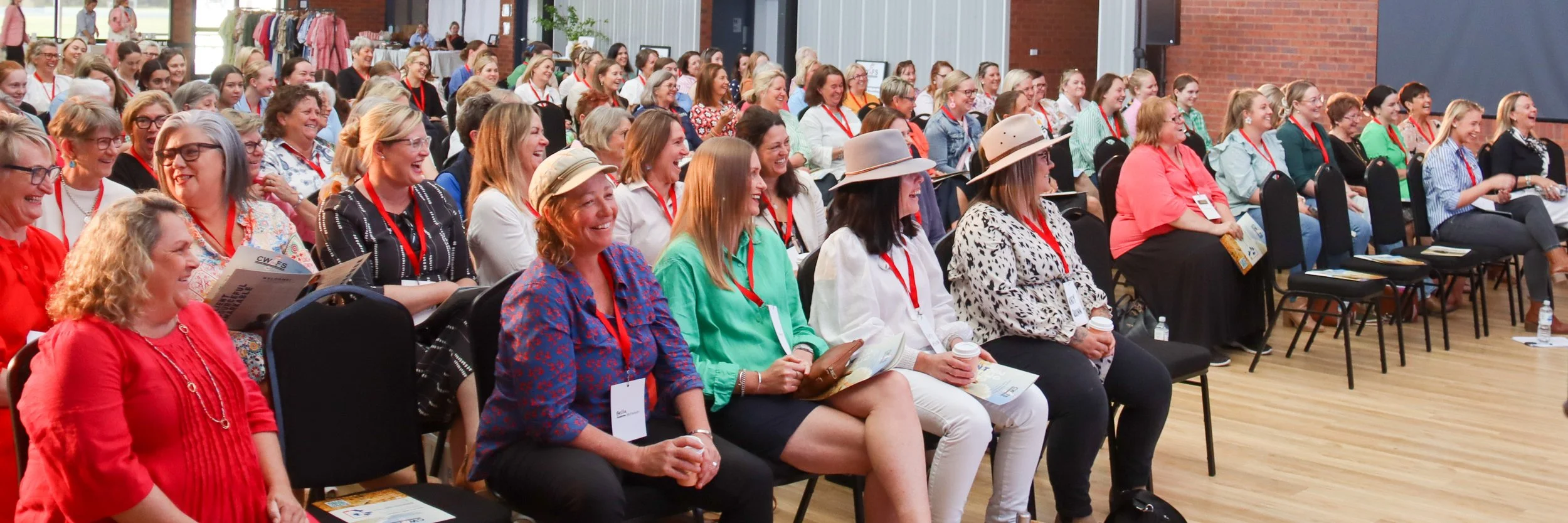 An audience of women sitting and laughing during a conference or seminar in a large, well-lit room.