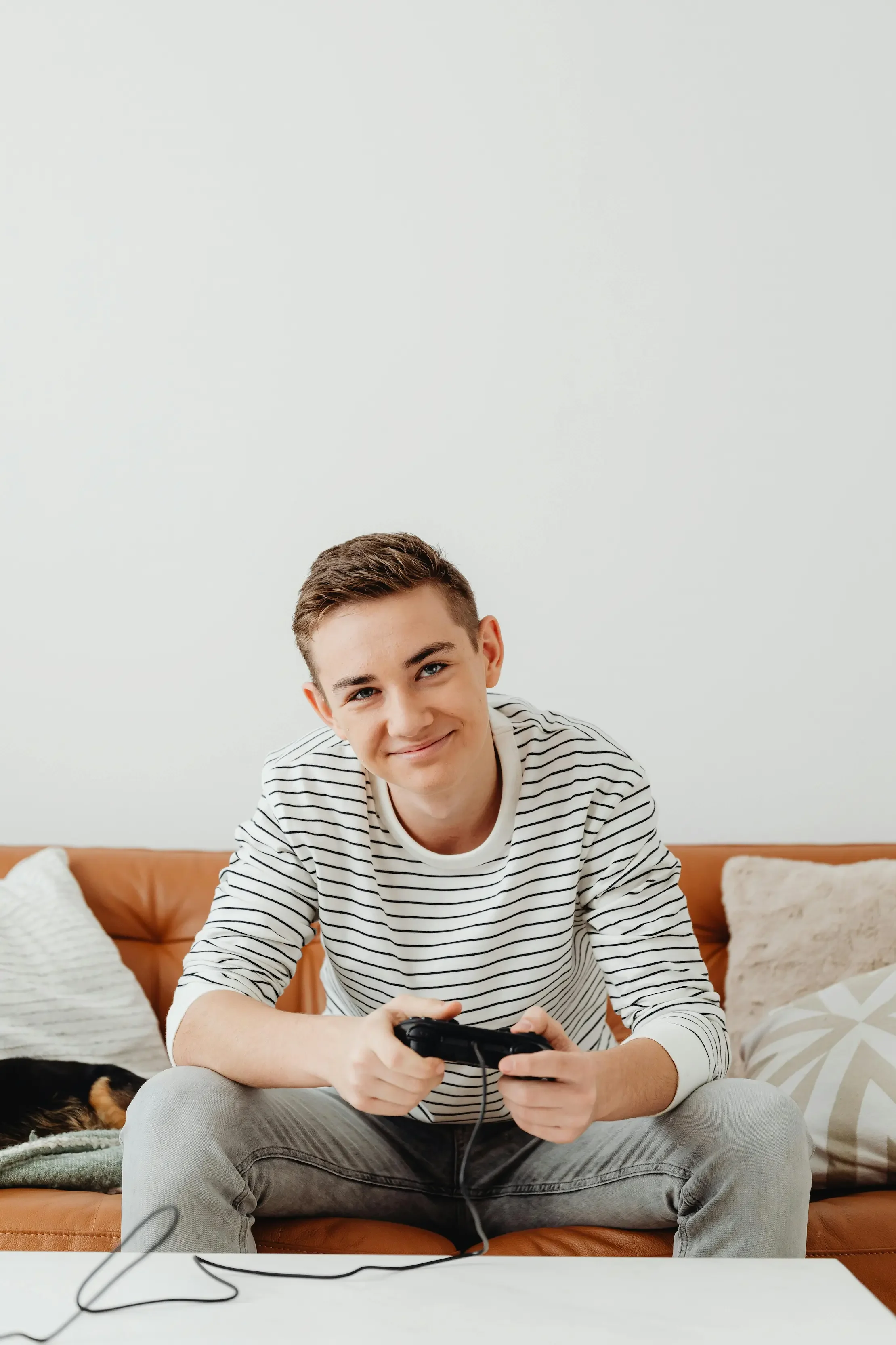 A smiling teenage boy sitting on a leather couch, holding a video game controller, representing a relaxed and approachable environment for teen therapy.