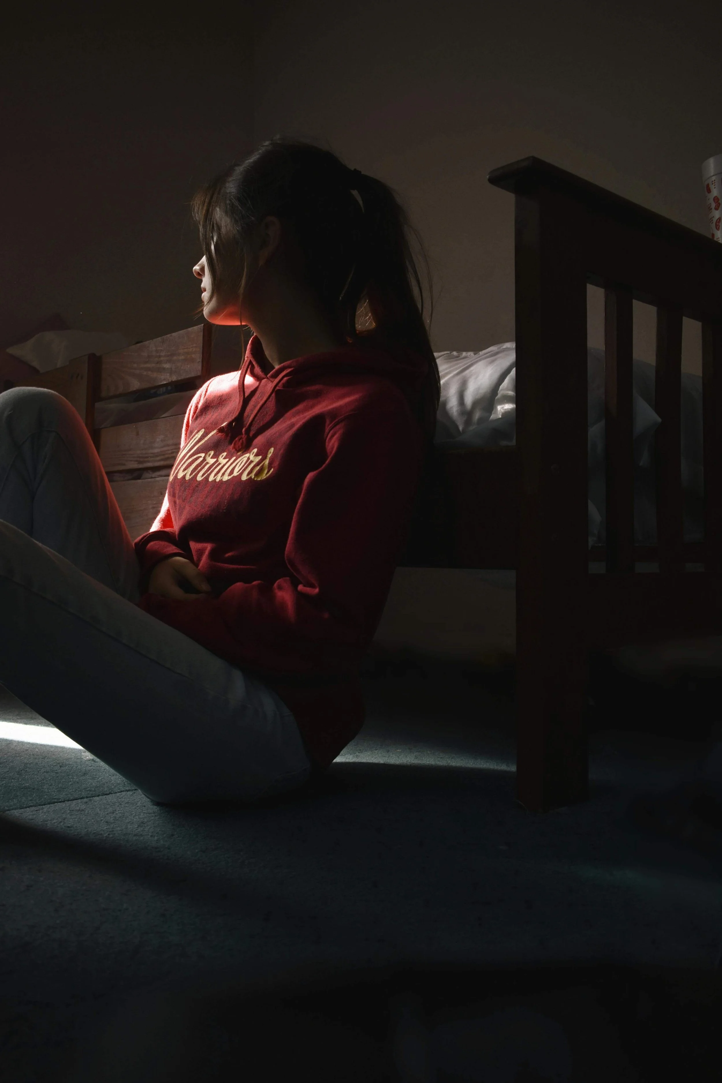 A young woman sitting in shadows by her bed, illustrating the isolation and quiet struggle often associated with depression or anxiety.