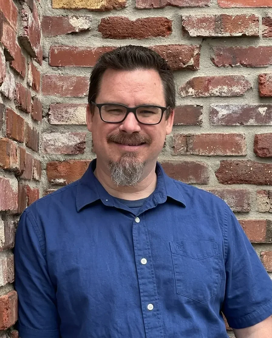 Portrait of John Opalka MA. LPC., a mental health therapist, smiling in front of a brick background.