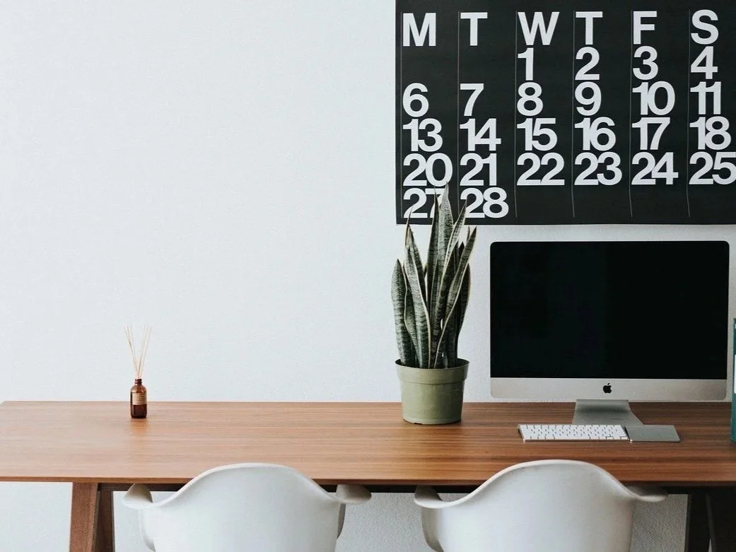 Office desk with a computer, potted snake plant, clock calendar, and reed diffuser holder.
