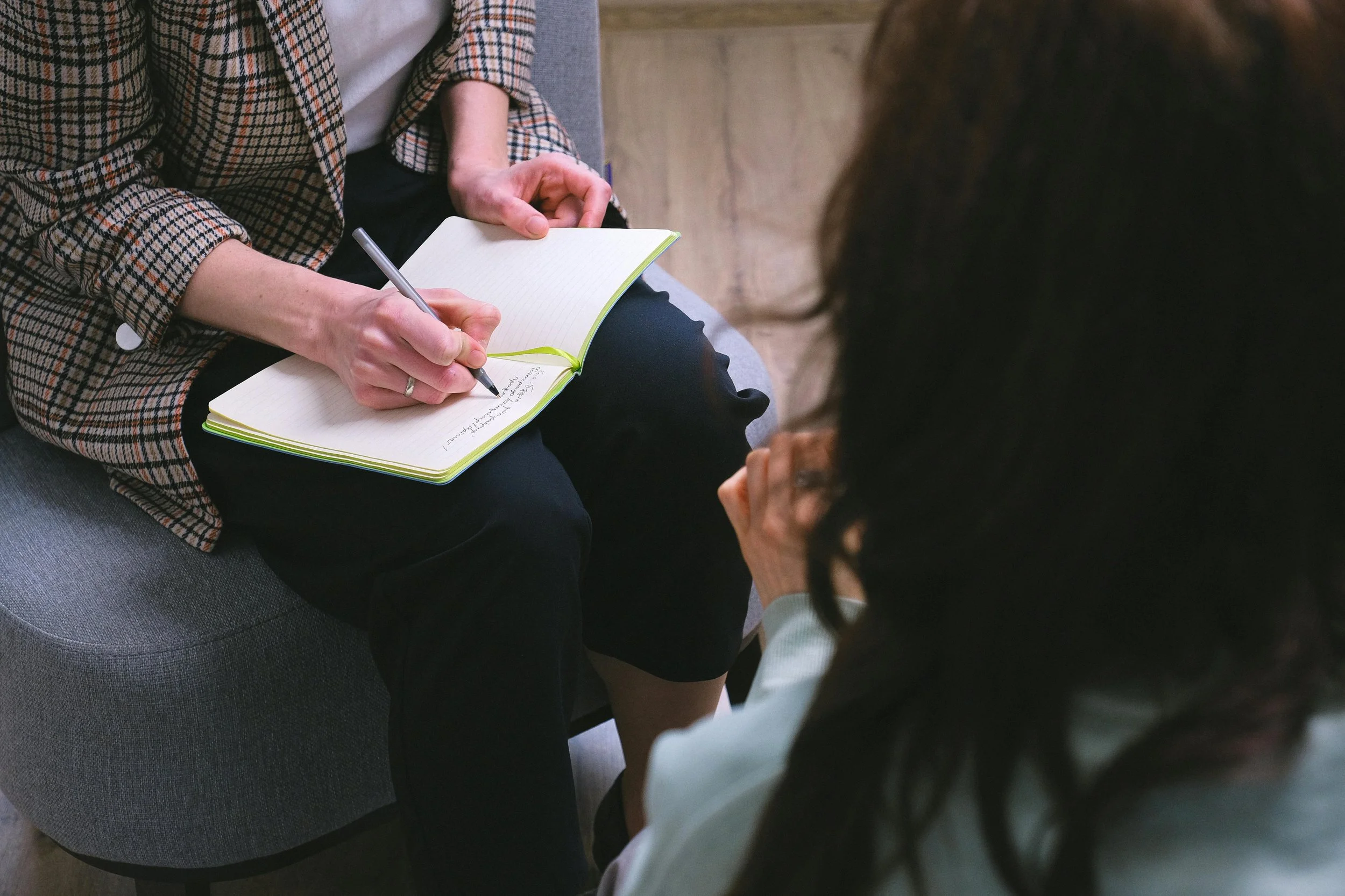 Woman in plaid sport jacket holding a notebook and pen going over counseling specialties with woman