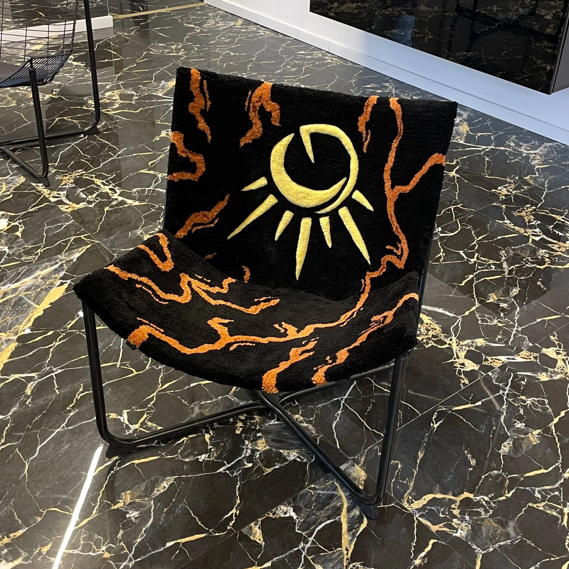 Black chair with a sun and moon design and orange flames, placed on a black marble floor with white and gold veins.