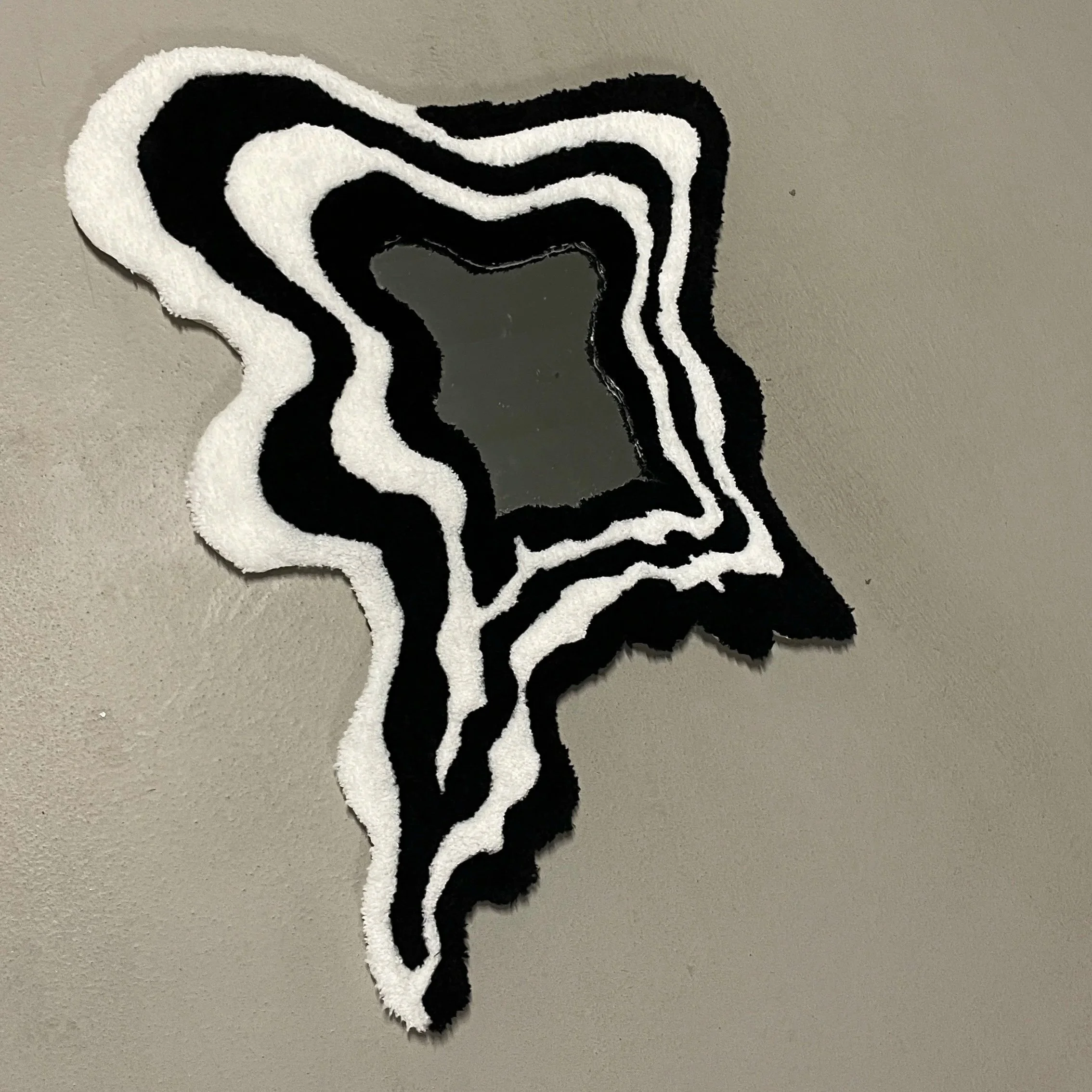 A decorative mirror with a black and white wavy, irregular border placed on a beige wall.