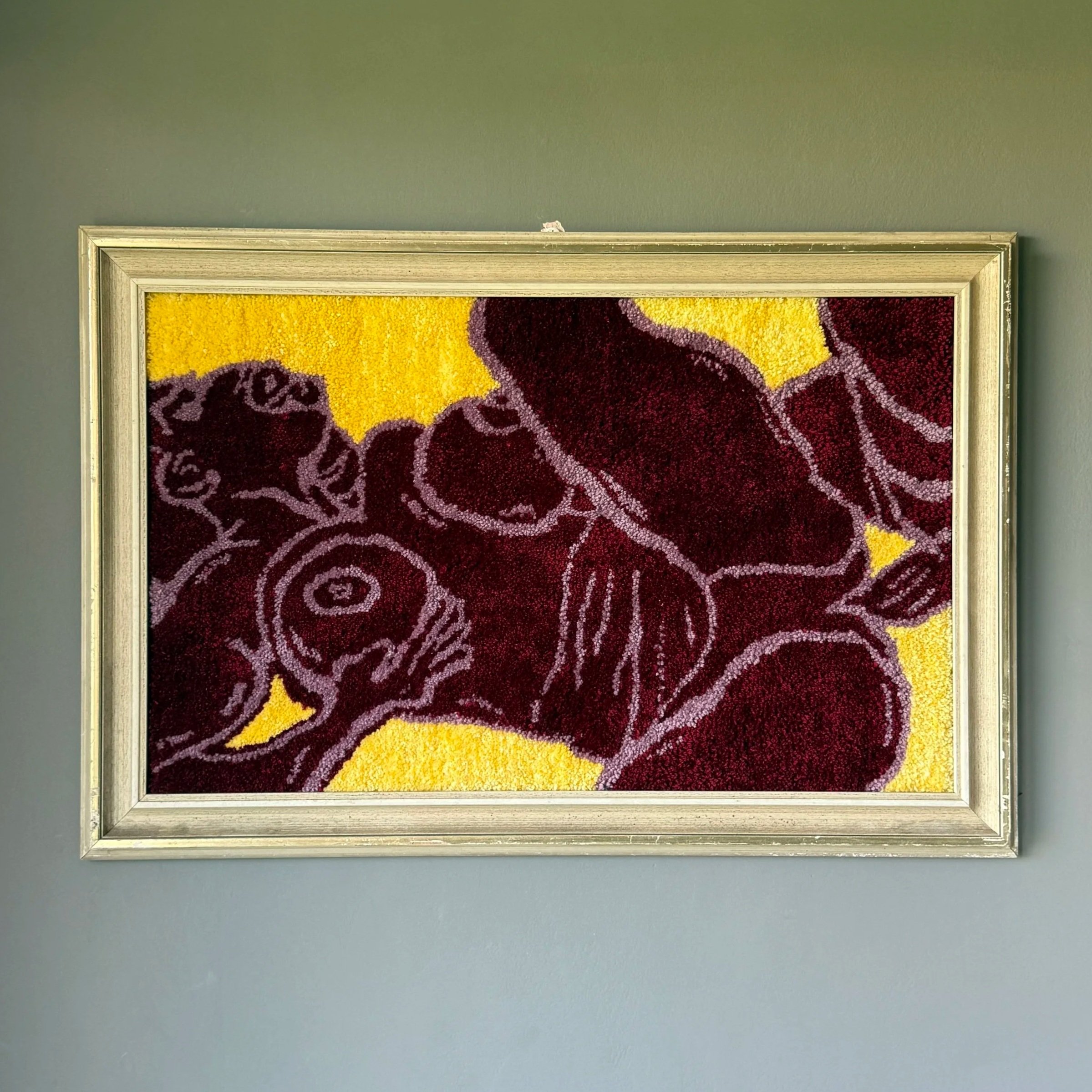 A framed artwork depicting an abstract floral design in dark purple or burgundy against a bright yellow background.