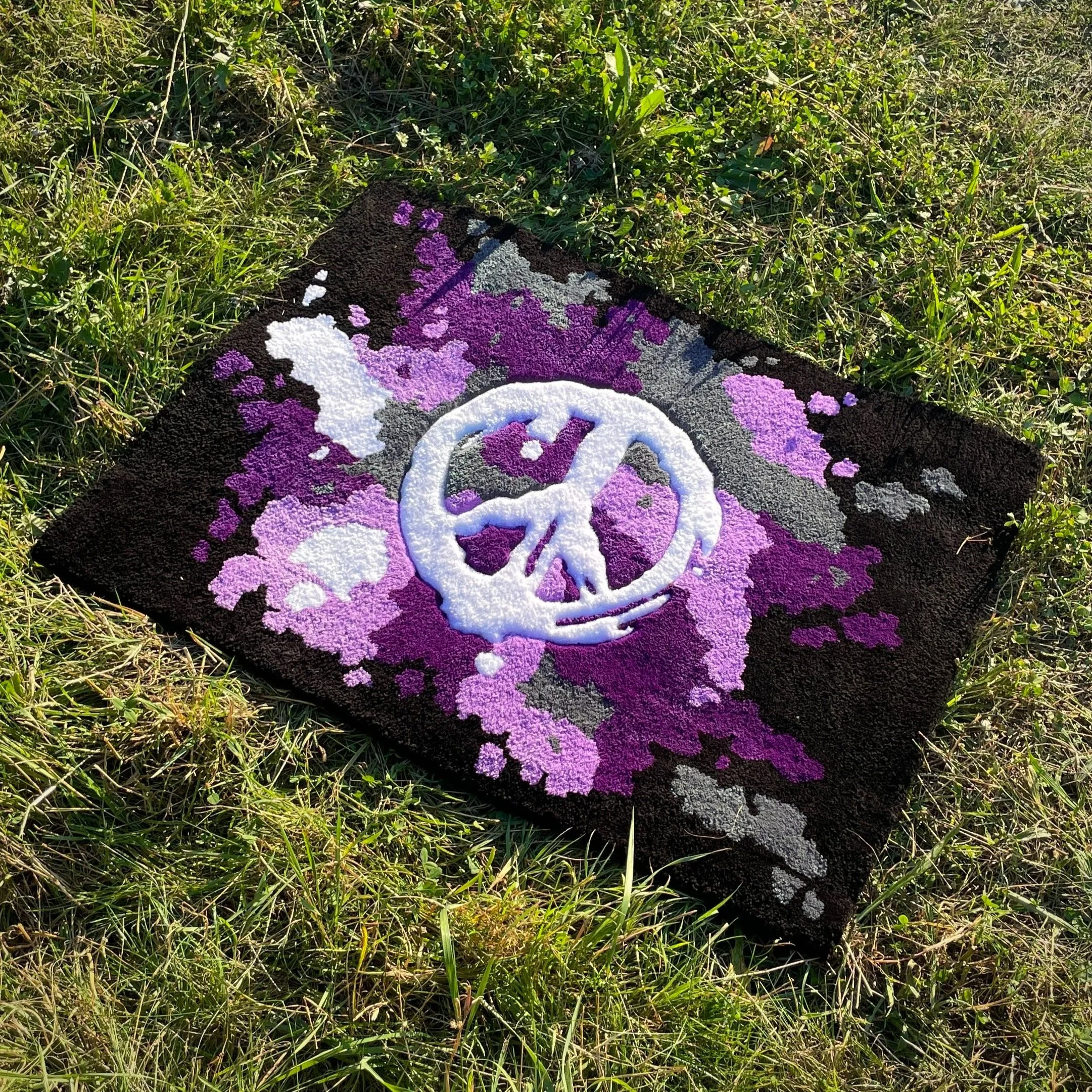 A colorful flower rug with a white peace sign in the center, lying on the grass outdoors.