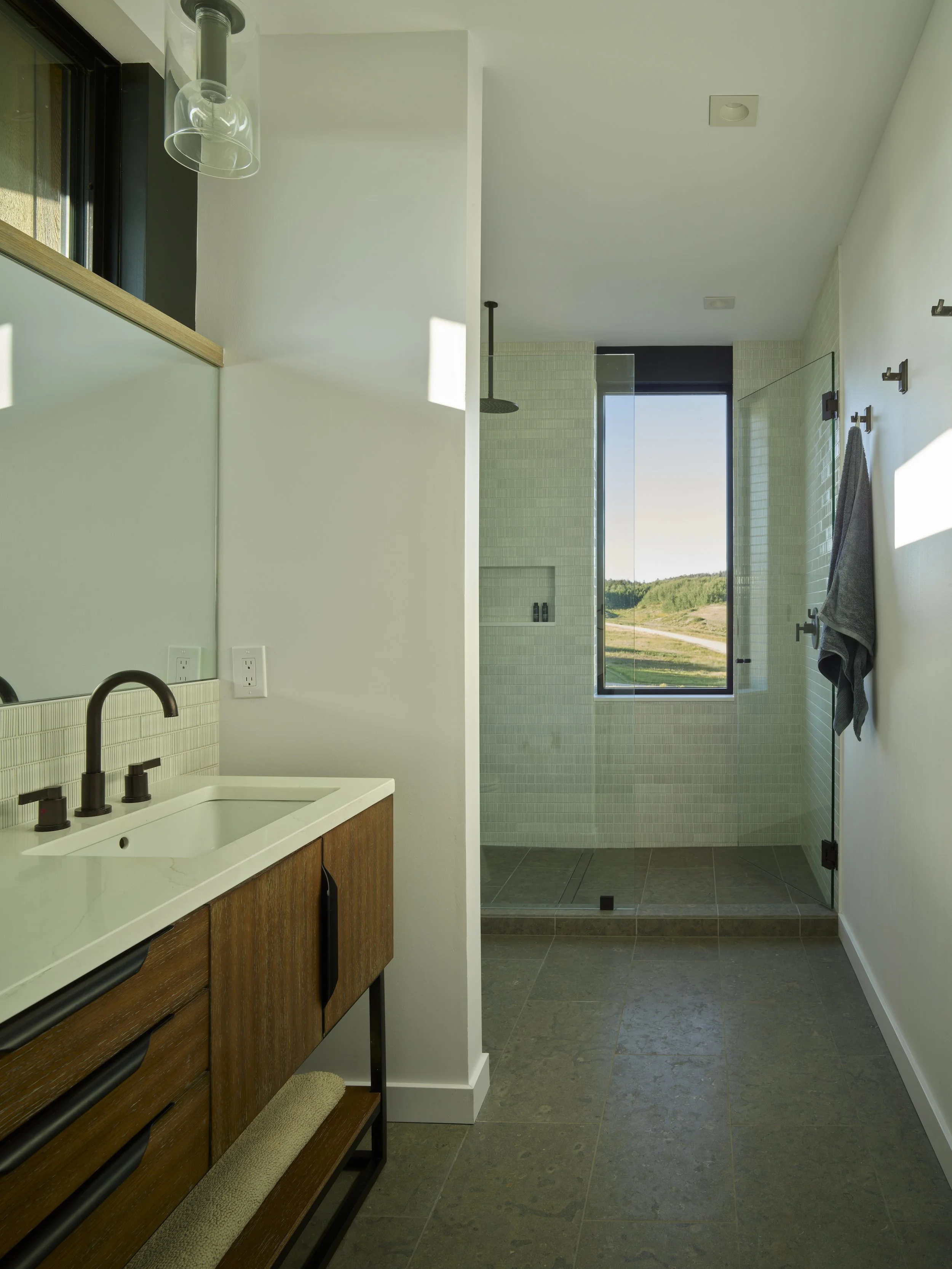 Modern bathroom with a white vanity, black fixtures, and a walk-in shower with a large window showing a landscape.