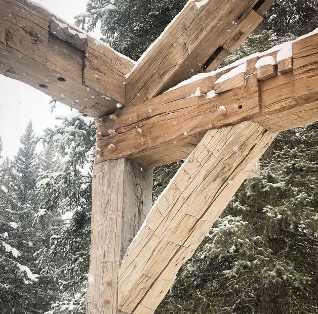 Close-up of a snowy wooden structure under construction, showing wooden beams and joints with snow in the background.