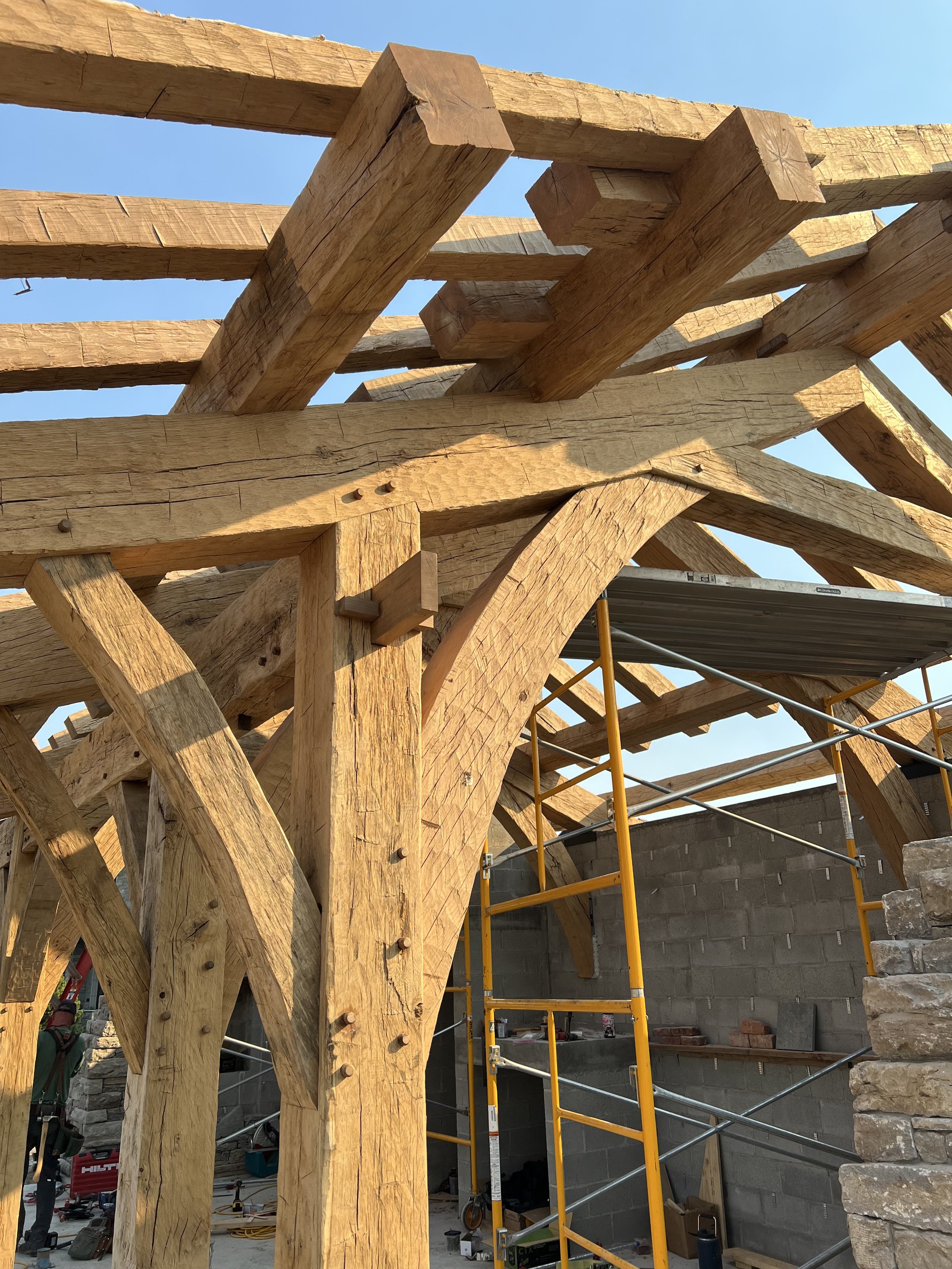 Close-up of a wooden roof framework under construction, showing large wooden beams and scaffolding with construction tools and materials inside a building