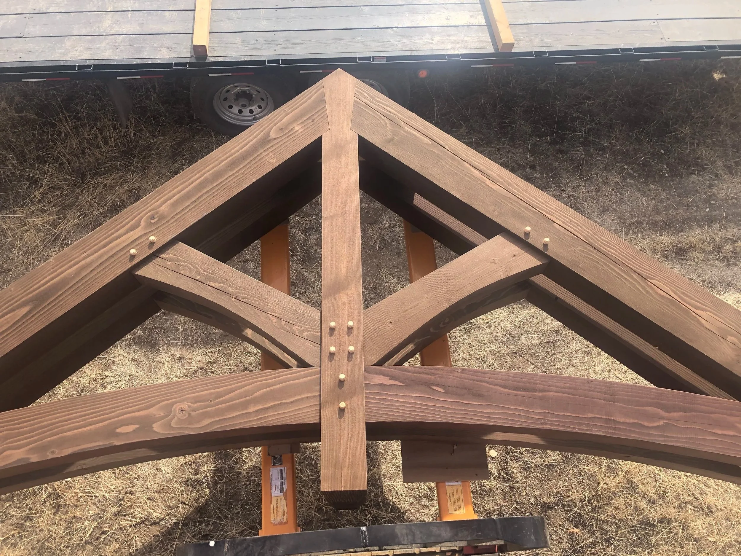 Unfinished wooden deck railing being assembled on a grassy area with a trailer in the background.