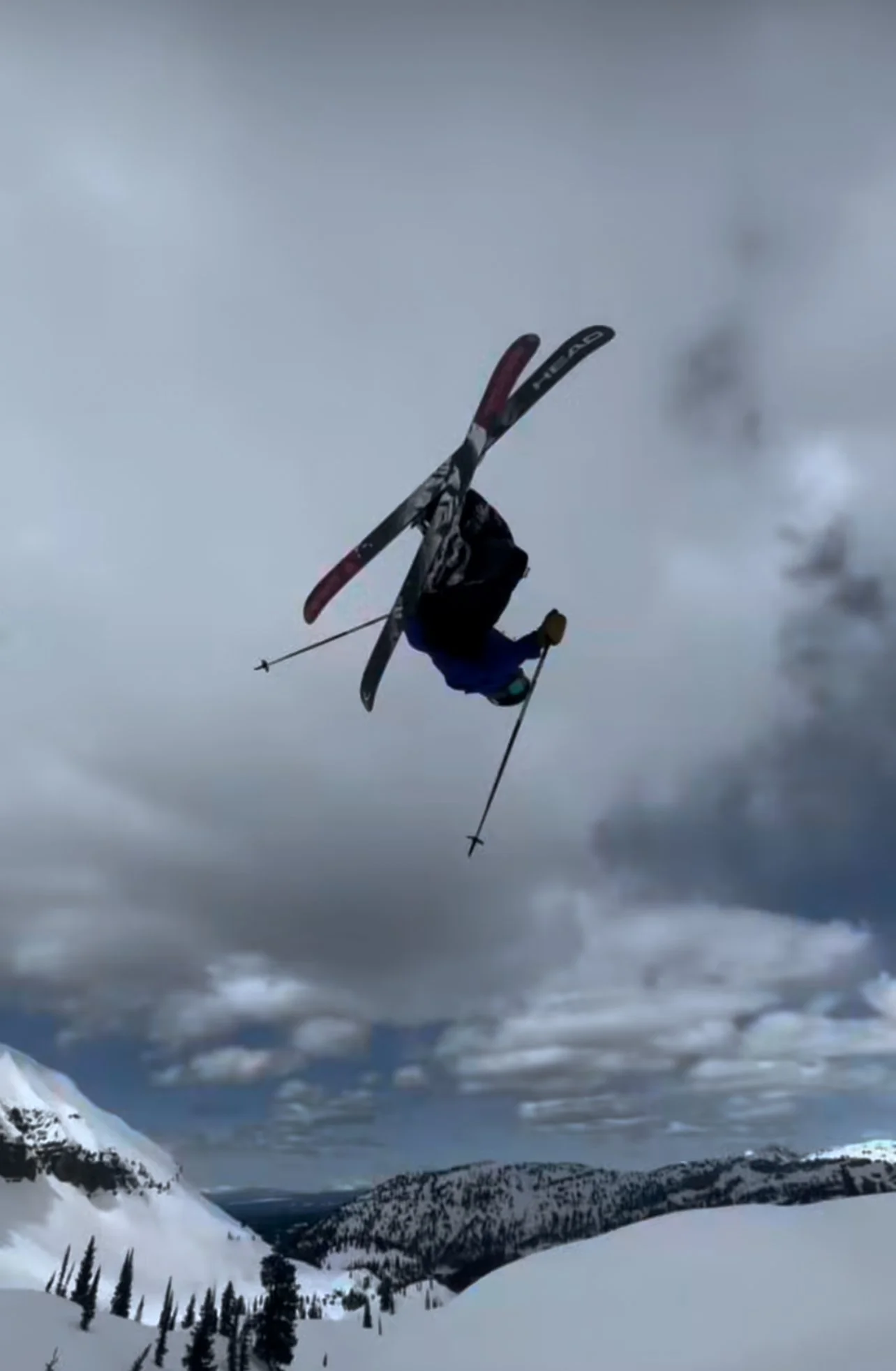 Skier performing a mid-air flip on a snowy mountain slope under cloudy sky.