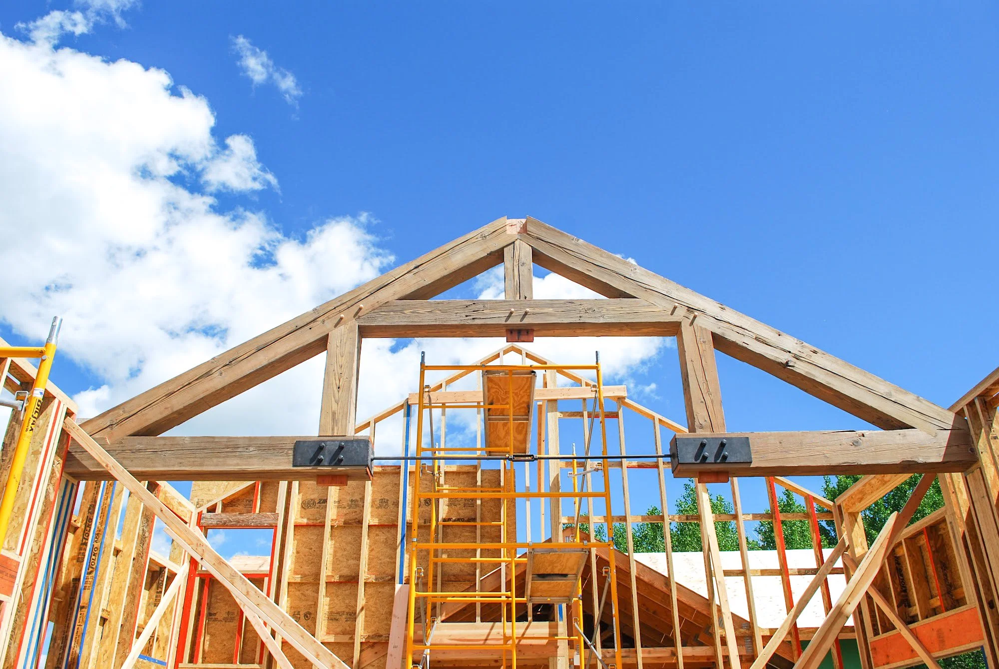 Construction site with wooden framing and scaffolding under a blue sky with clouds.