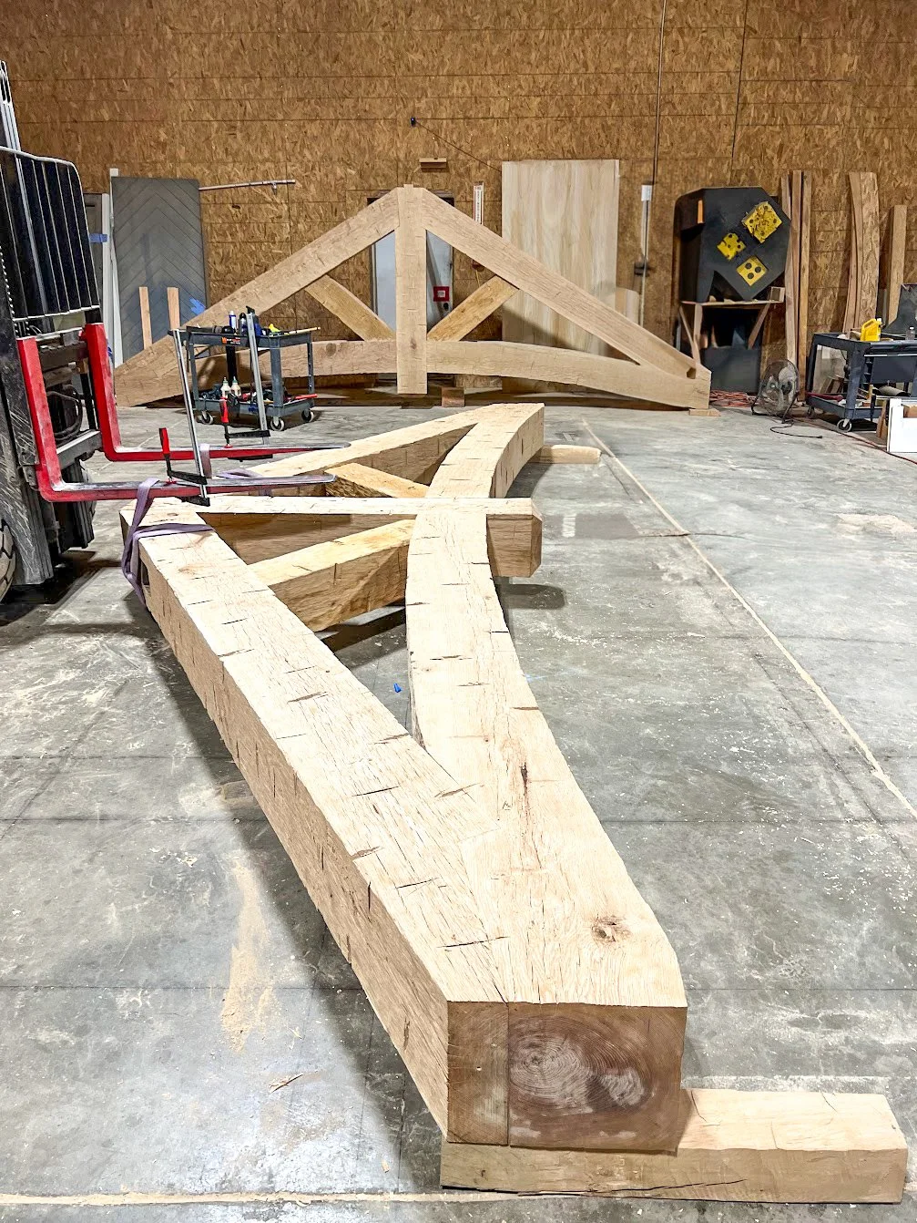 Large wooden framework in a workshop with tools and equipment, on a concrete floor.