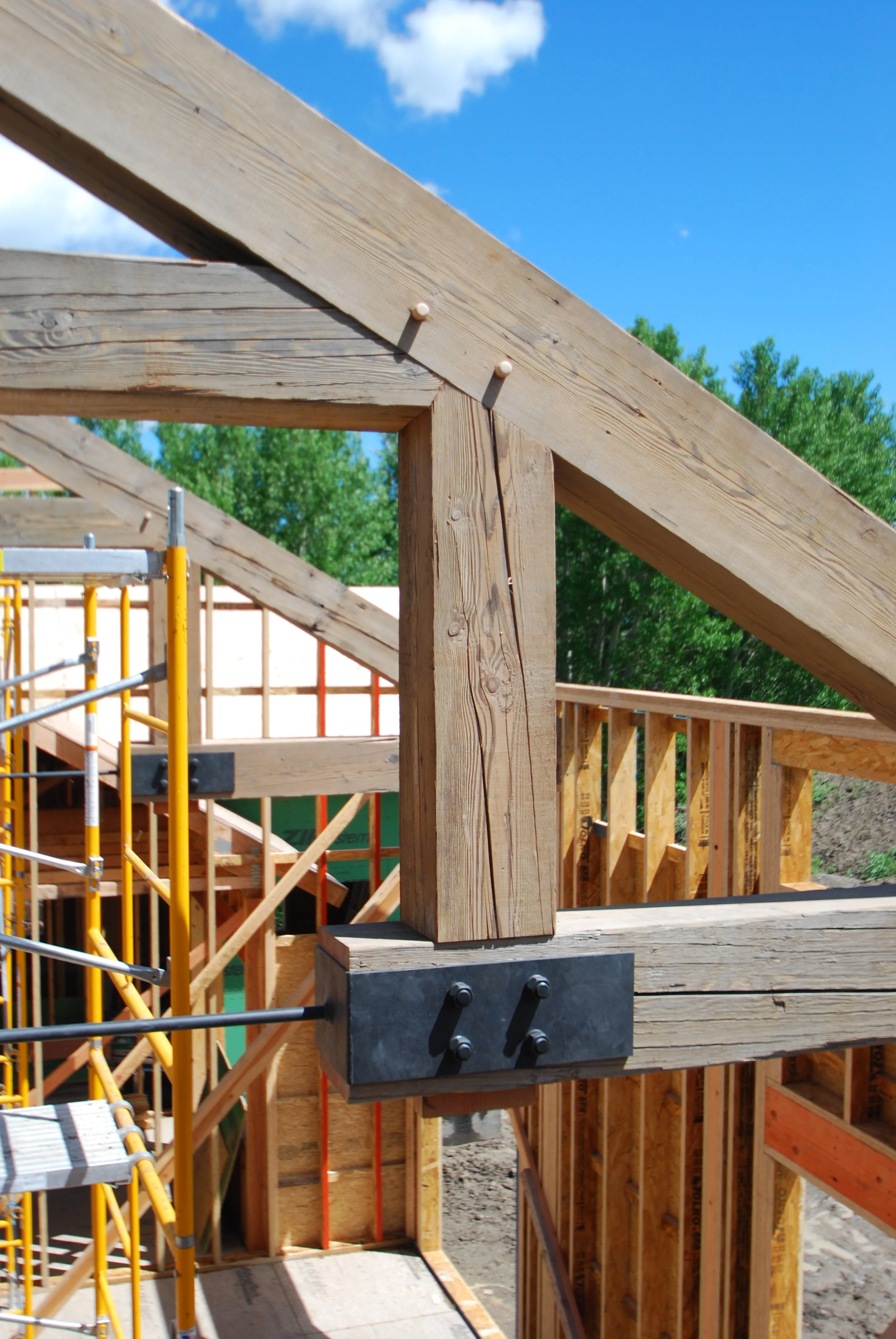Close-up of a wooden staircase railing under construction at a building site, with a blue sky and green trees in the background.